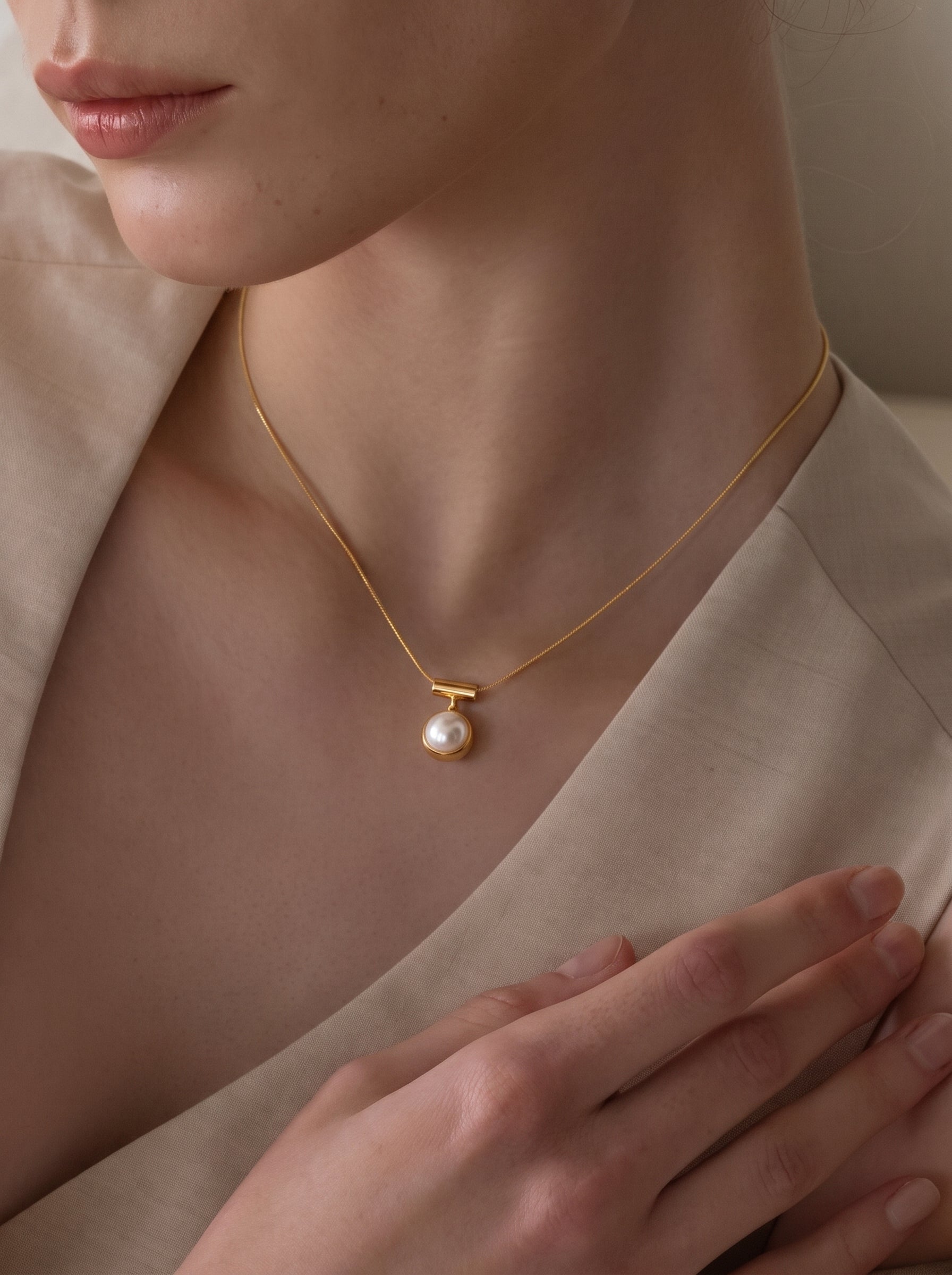Close-up of a model wearing the Glimpse Freshwater Pearl Pendant Necklace, featuring a single lustrous 10mm round white pearl suspended from a gold-toned horizontal bar on a delicate chain. @model