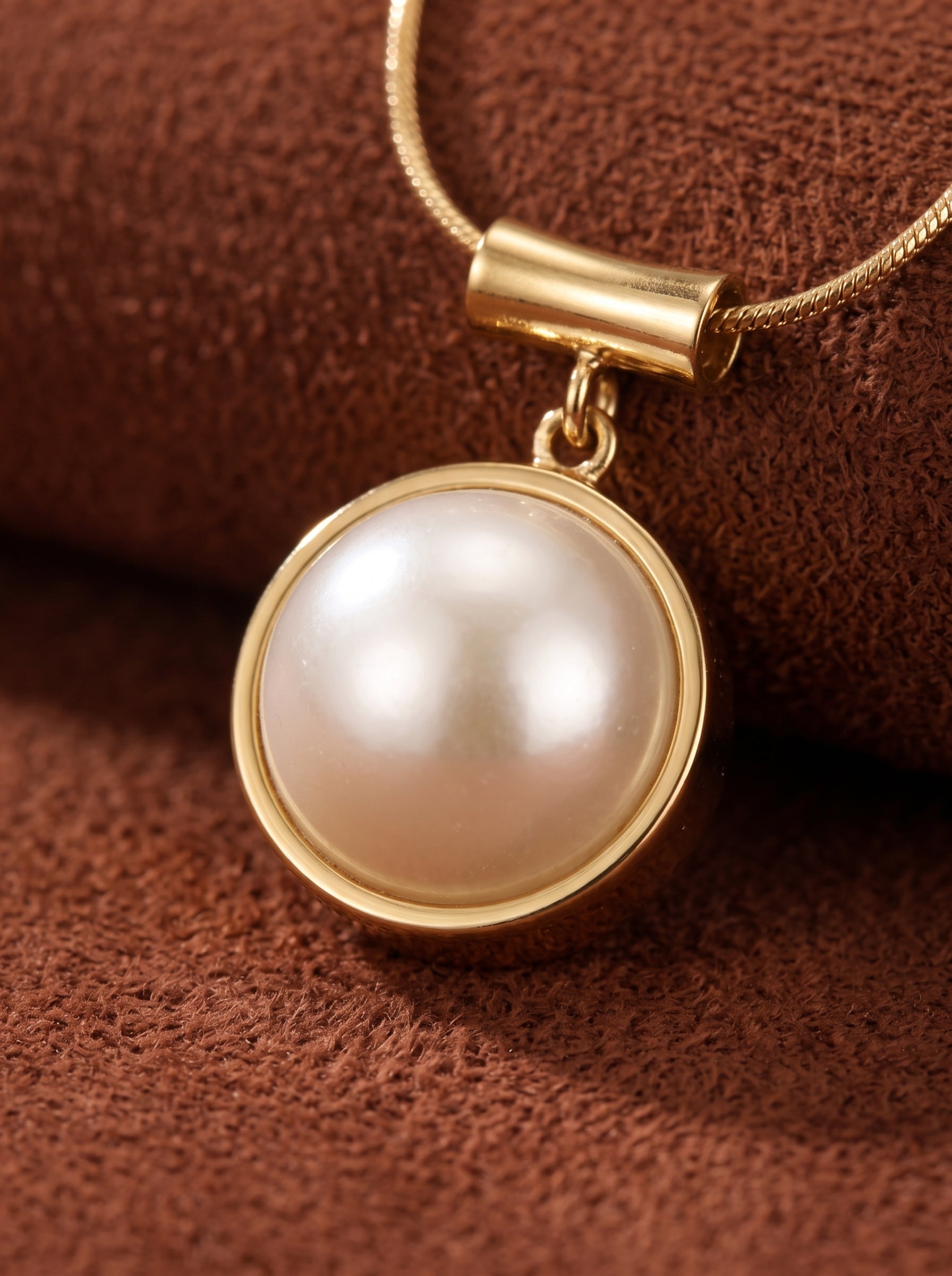 Glimpse - Round White Freshwater Pearl pendant necklace with gold-toned bezel and chain on a brown textured background. @pearl