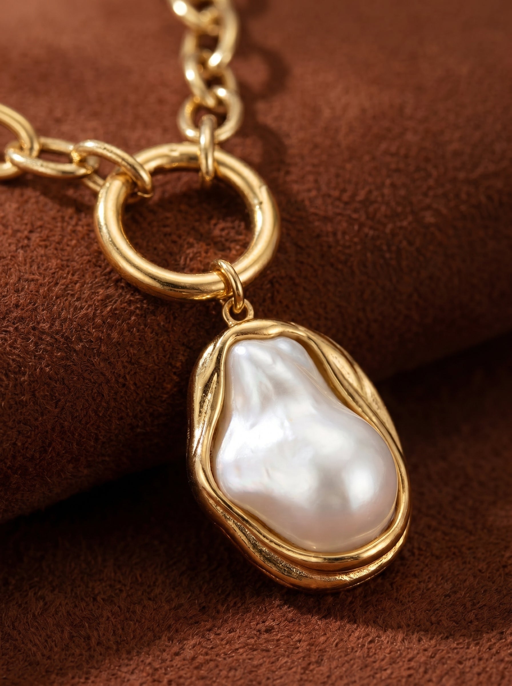 Close-up of a chunky gold-toned chain necklace featuring a large, irregular white freshwater pearl pendant with a fluid, organic gold setting. The pearl has a natural luster and baroque shape, suspended from a circular link. @pearl
