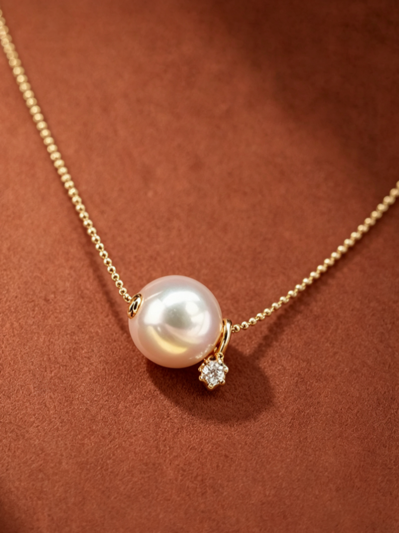 A close-up of a "Halo - Akoya Pearl Star Floating Necklace" featuring a lustrous 8mm white Akoya pearl with pink overtones, suspended on a delicate gold chain. A small, sparkling diamond star charm dangles beside the pearl.