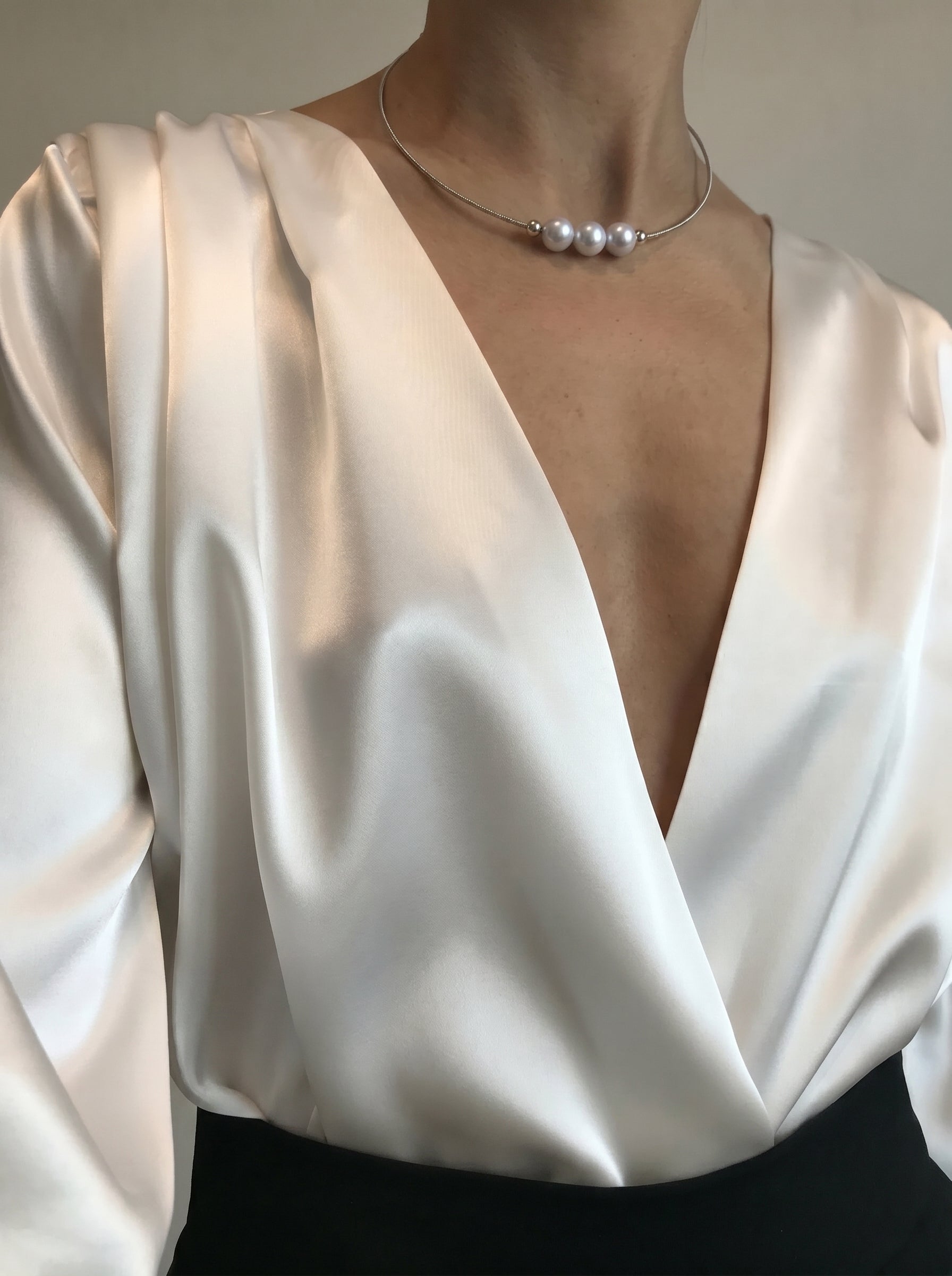 A woman wearing a white satin blouse and black skirt, adorned with the Haze Akoya Pearl Floating Chain Necklace featuring three lustrous pearls on a delicate silver chain. @lifestyle