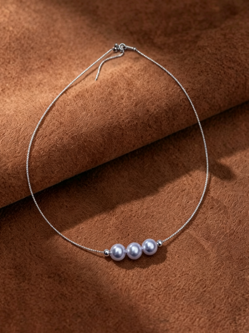 Haze necklace featuring three 8mm Akoya pearls with a silver-blue hue, appearing to float on a delicate, thin silver chain, displayed against a textured brown background.