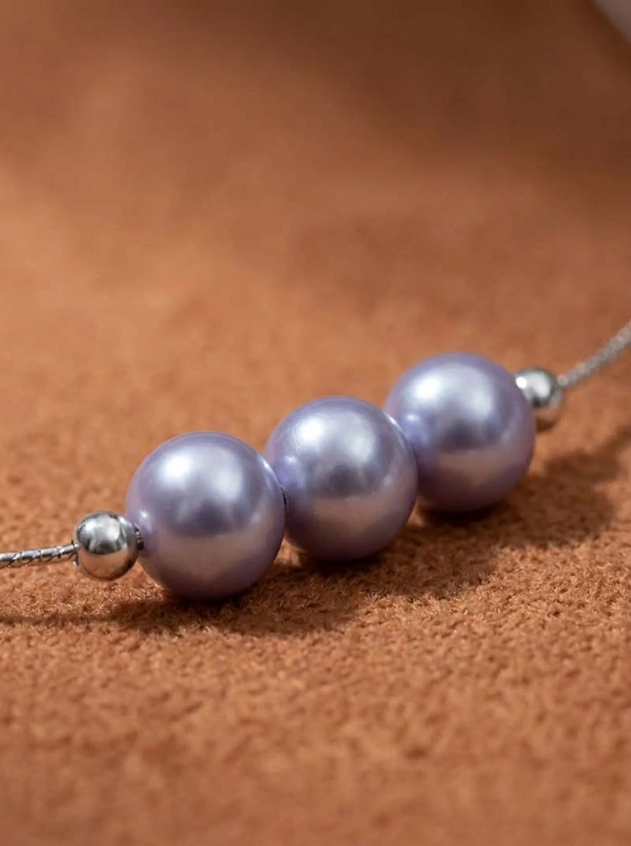Close-up of the Haze Akoya Pearl Floating Chain Necklace, featuring three lustrous lavender pearls with silver accents on a delicate chain against a textured brown background @pearl