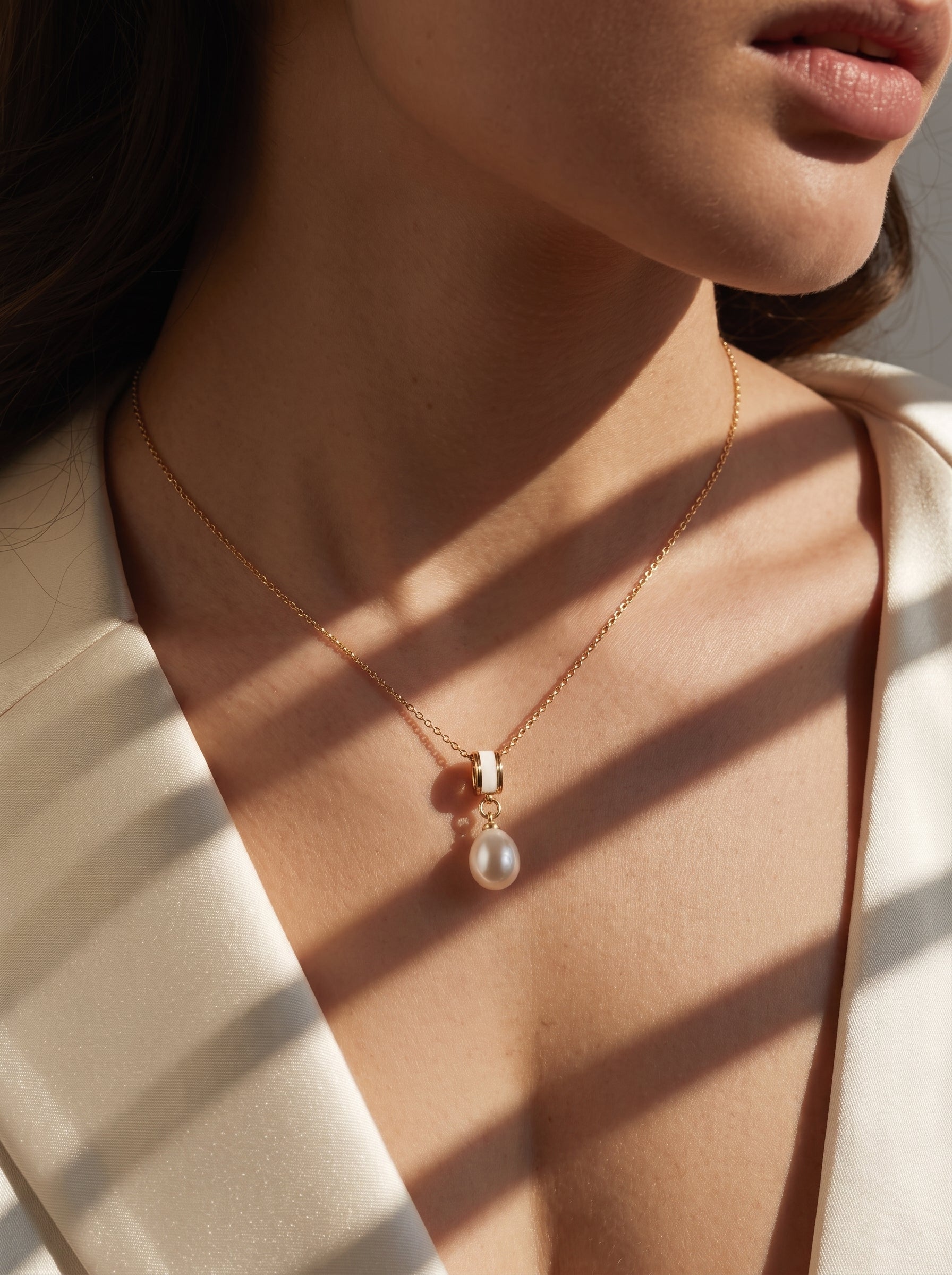 Close-up of a woman wearing the Inner Glow Freshwater Pearl Drop Pendant Necklace, featuring a single white pearl on a gold chain with a cylindrical accent. @model