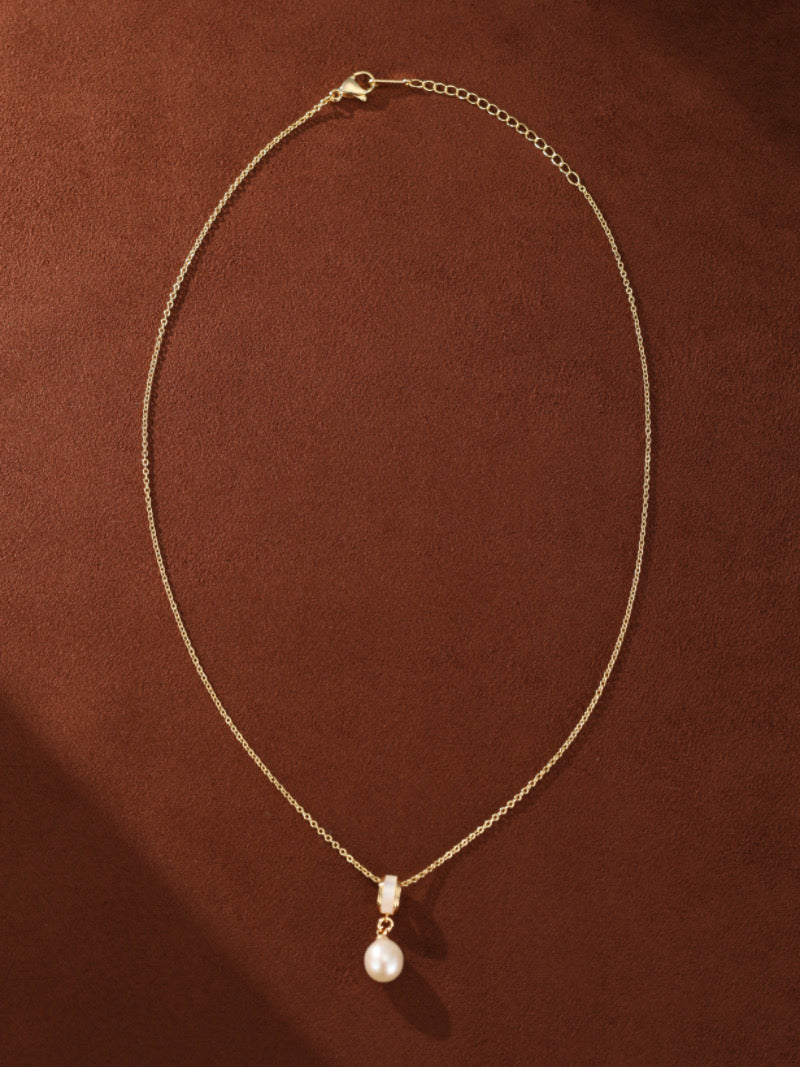 A gold-toned delicate chain necklace with a single, luminous white freshwater pearl drop pendant accented by a contemporary cylindrical element.