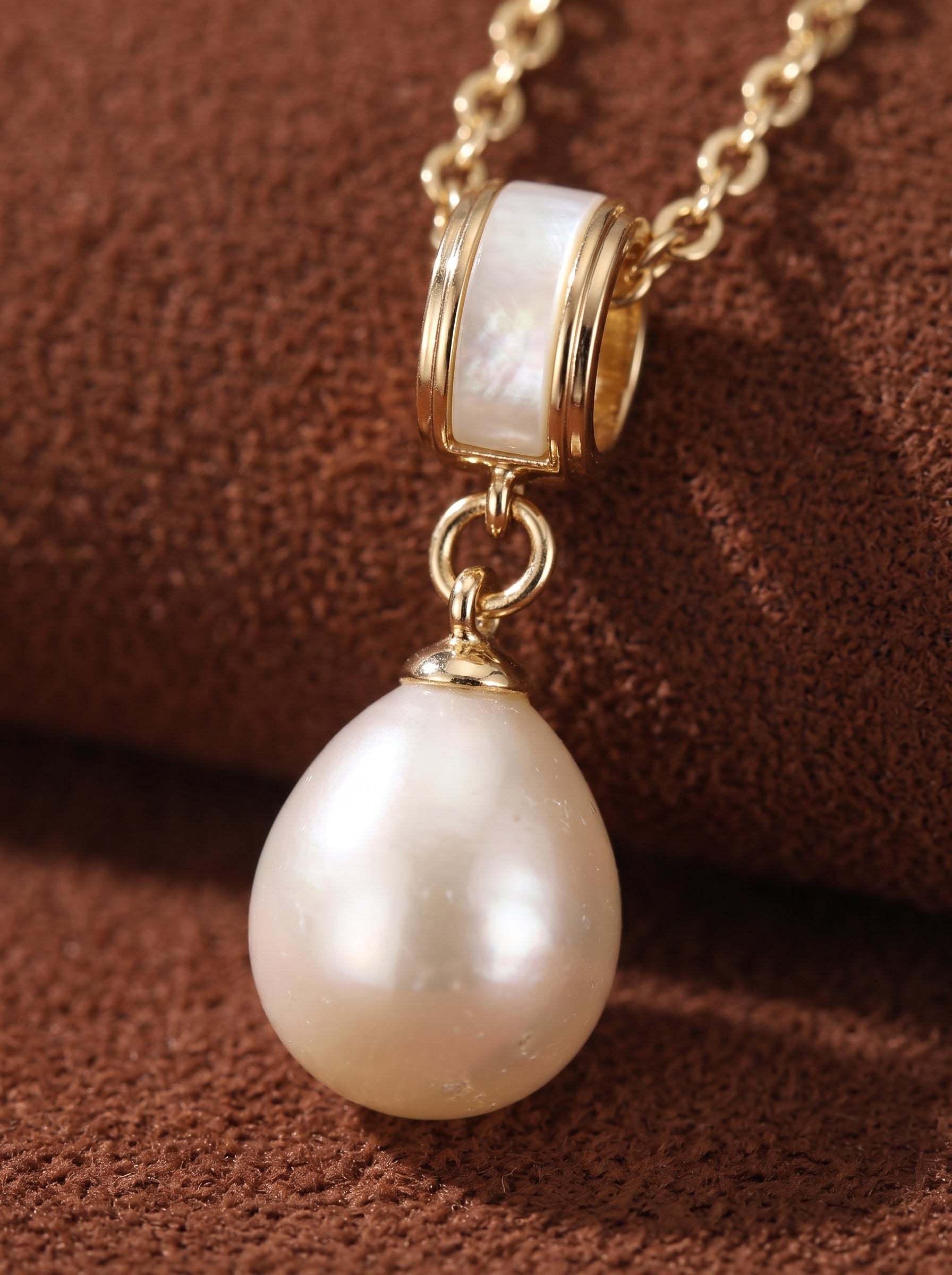 Close-up of a delicate gold chain necklace featuring a single, luminous white freshwater pearl drop pendant accented by a modern cylindrical element. @pearl