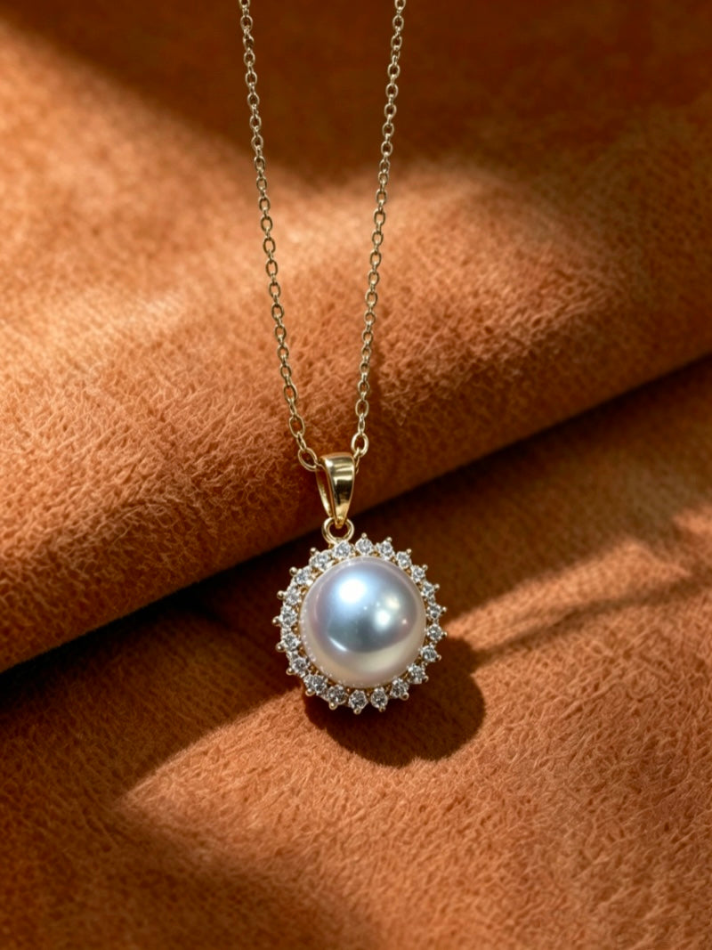 A delicate gold chain necklace featuring a large, lustrous Akoya pearl surrounded by a halo of sparkling diamonds, set against a textured brown background.