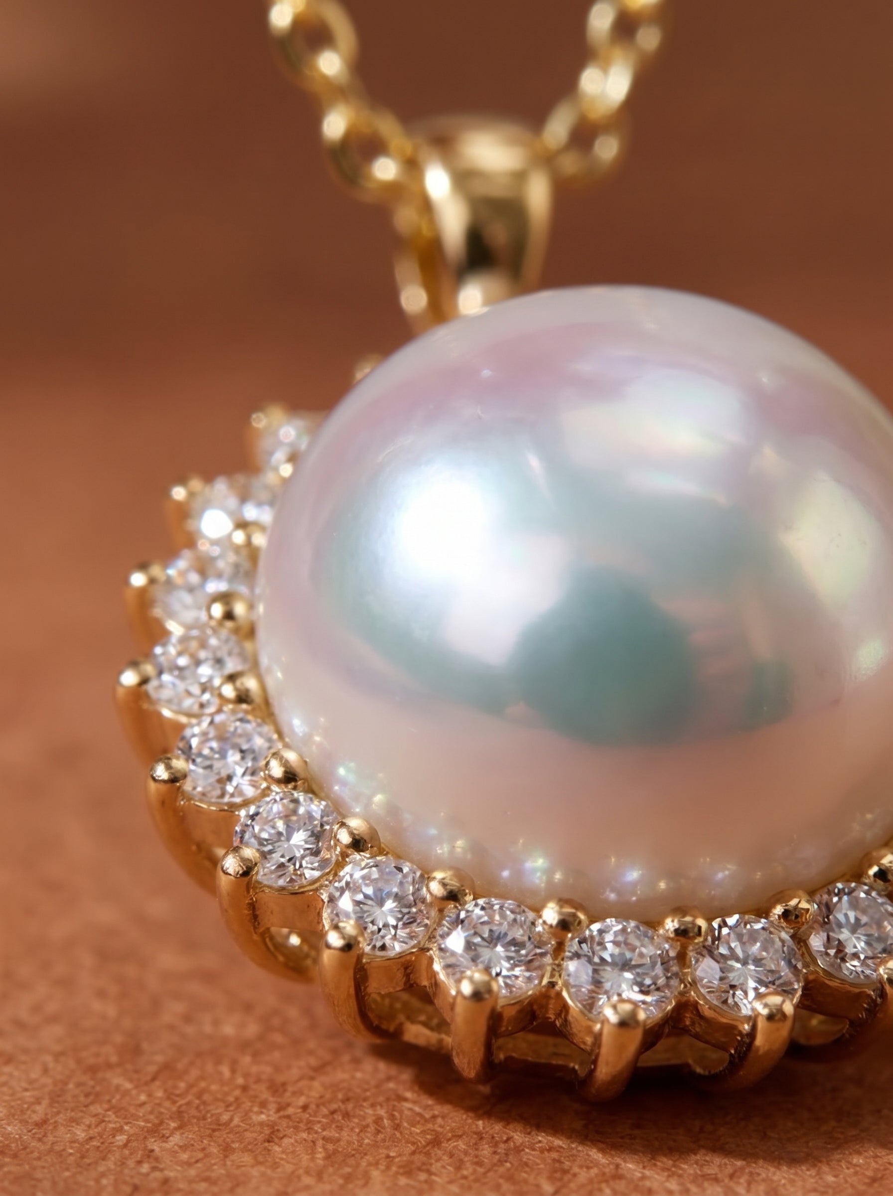 Close-up of a 9mm round Akoya pearl necklace with a halo of brilliant-cut diamonds set in gold, evoking a sunburst design. The pearl has iridescent silver and blue overtones. @pearl