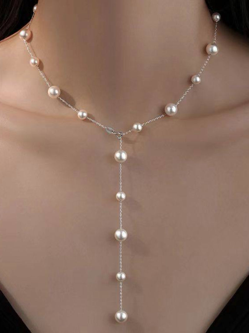 Close-up of a woman wearing a delicate silver chain necklace with a station design, featuring alternating 8mm and 4mm white imitation pearls, and a dangling pendant of pearls.
