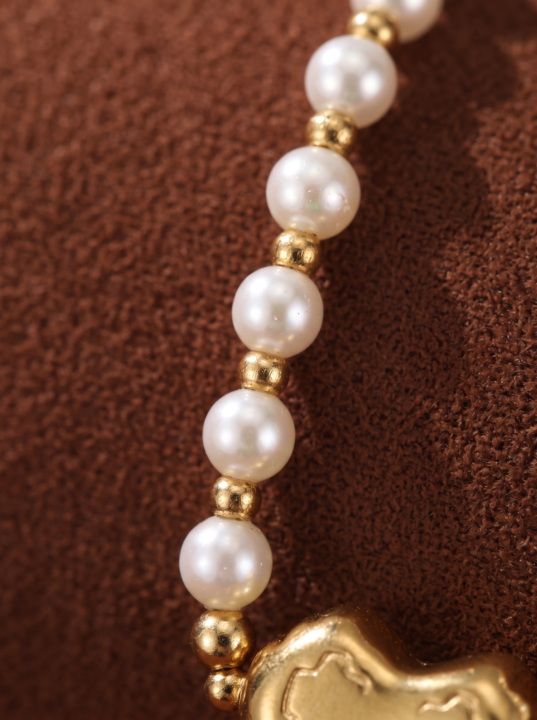 Close-up of a Kindred freshwater pearl necklace featuring a delicate chain of 3 mm white pearl beads interspersed with gold-tone accent beads, leading to a gold-tone heart pendant. @pearl