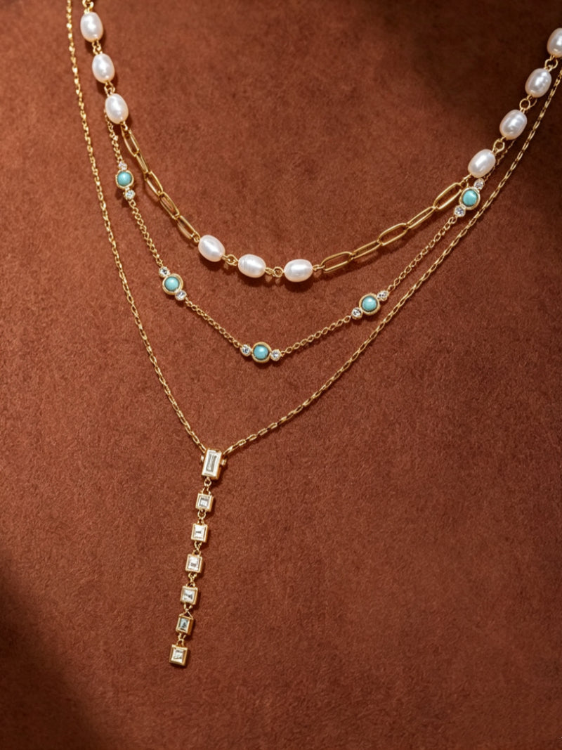 Lagoon Layers necklace featuring a layered design with white freshwater pearls, turquoise beads, and cubic zirconia stones, culminating in a cascading drop pendant of baguette and square-cut clear stones.