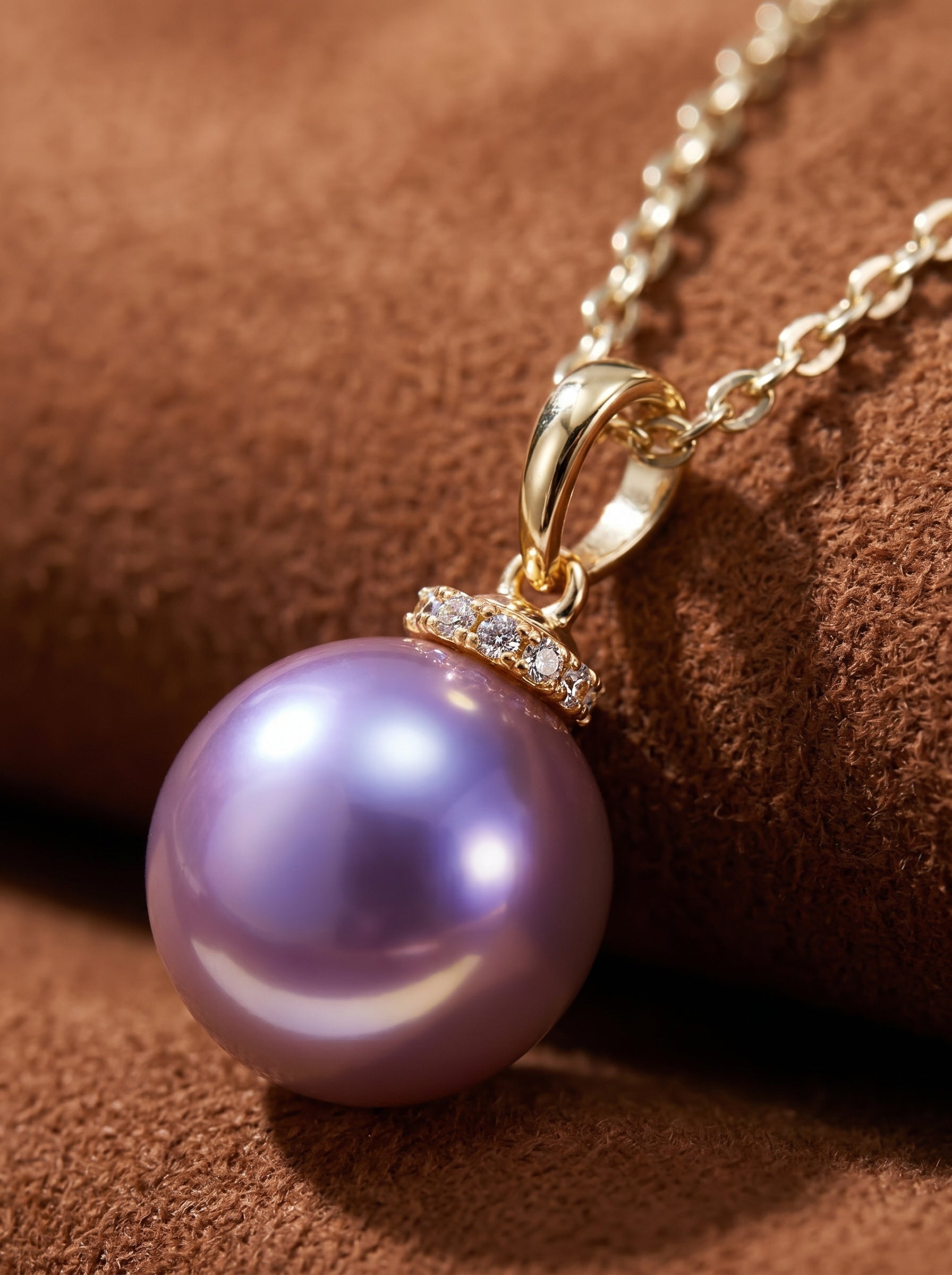 Close-up of a Lila Drop necklace featuring a lustrous round purple freshwater pearl suspended from a delicate gold chain, accented with a halo of small crystals.