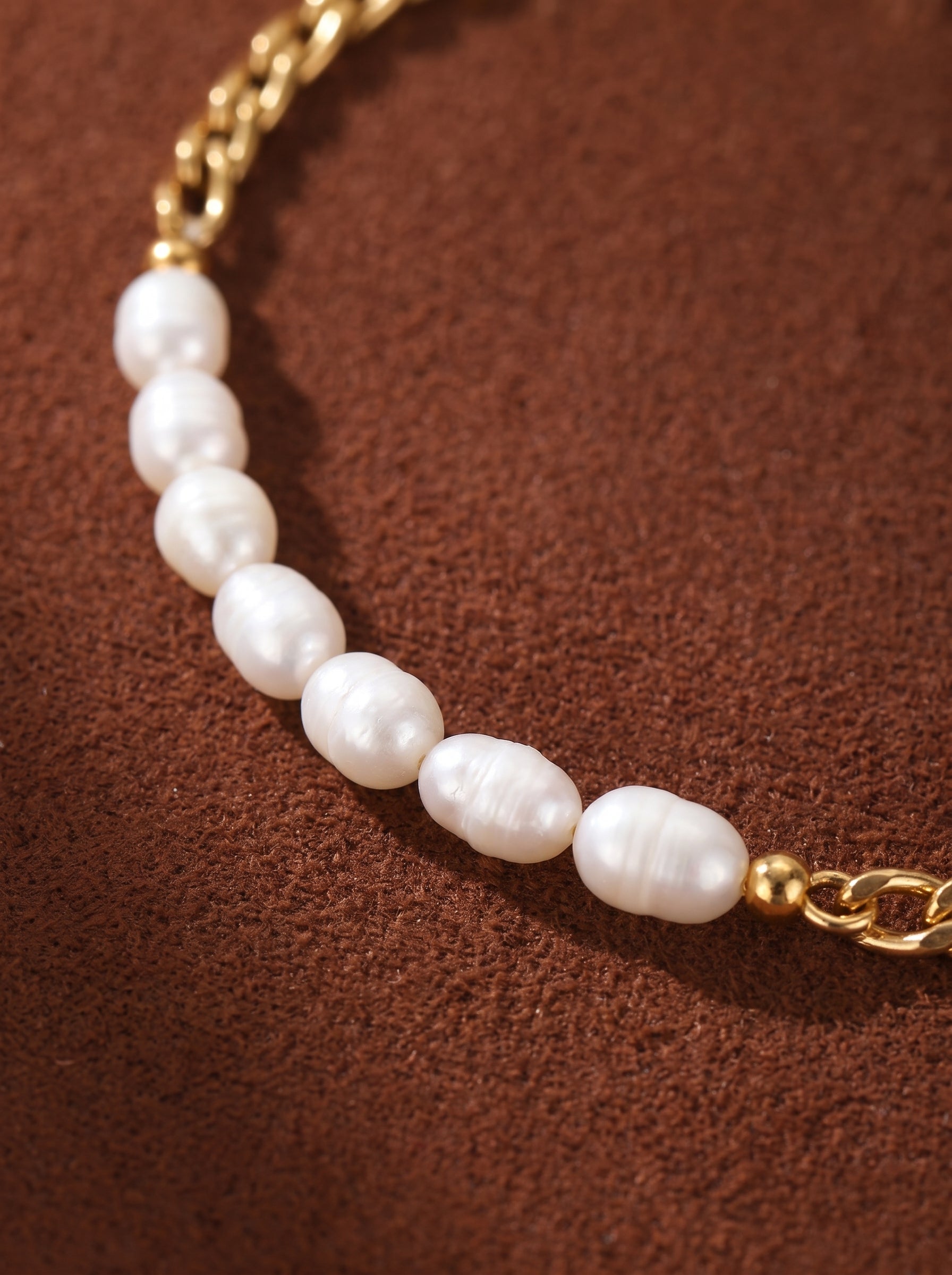 Linkage bracelet featuring a gold-tone curb chain alternating with oval freshwater pearls on a brown textured background. @pearl