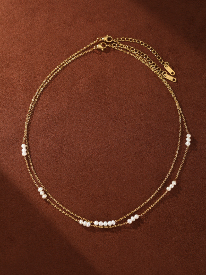 Un délicat collier superposé avec deux chaînes ton or ornées de petites perles blanches d'eau douce espacées.
