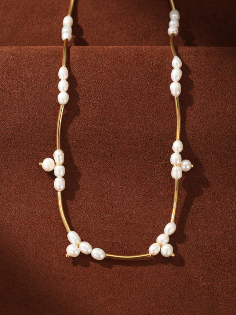 Lumen Cluster choker necklace with a thin gold bar adorned with clusters of white freshwater pearls resembling stars, presented on a textured brown surface. @pearl