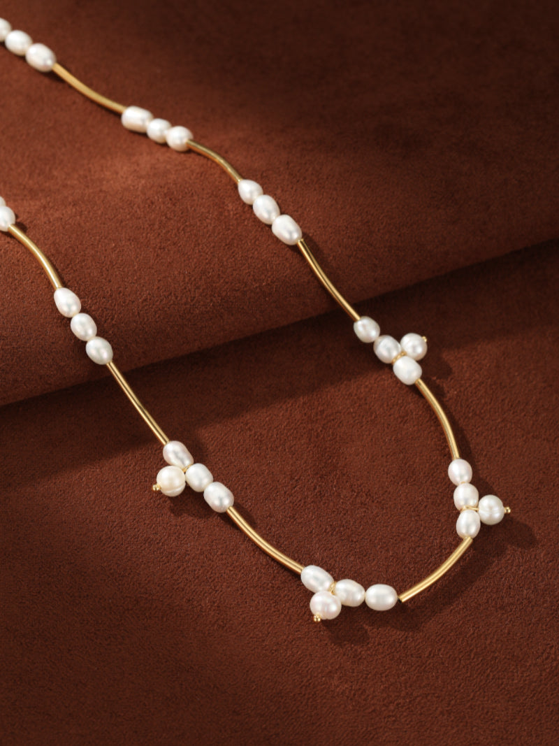 Lumen Cluster choker necklace with a thin gold chain and clusters of small white freshwater pearls arranged in a star-like pattern on a brown textured background. @pearl