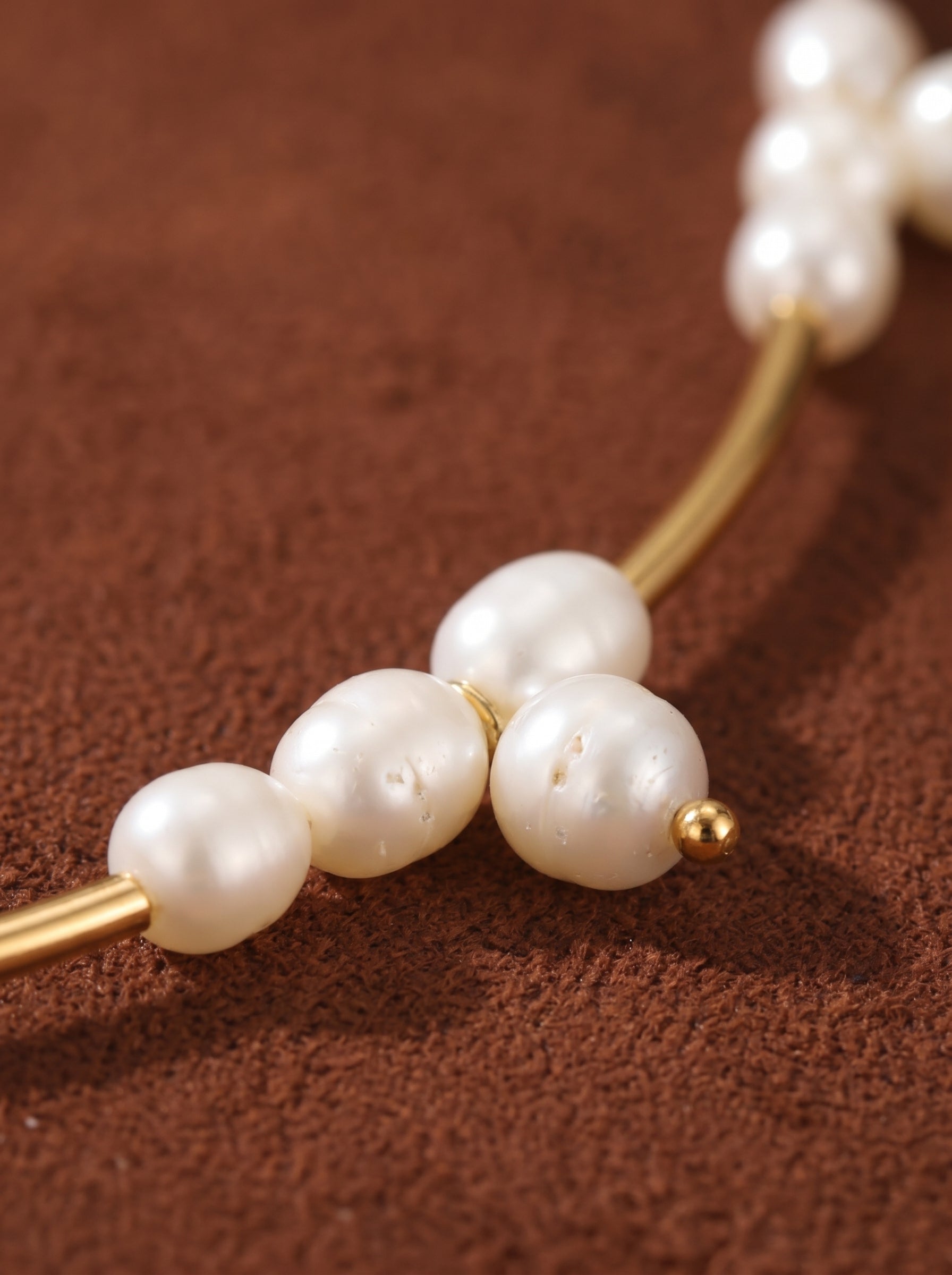 Close-up of the Lumen Cluster choker necklace with irregular white freshwater pearls clustered on a thin gold bar, accented by a small gold bead, against a textured brown background.@pearl