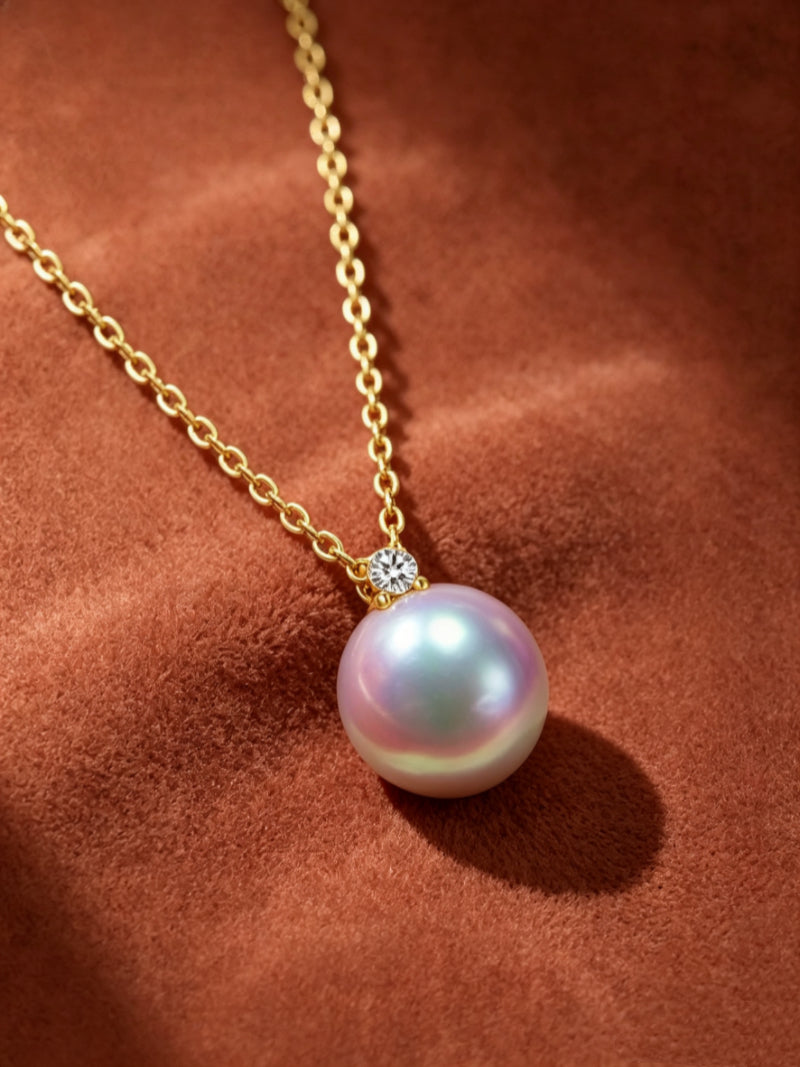 A delicate gold chain necklace featuring a single, lustrous Akoya pearl with pink and white overtones, accented by a small brilliant detail at the bail.