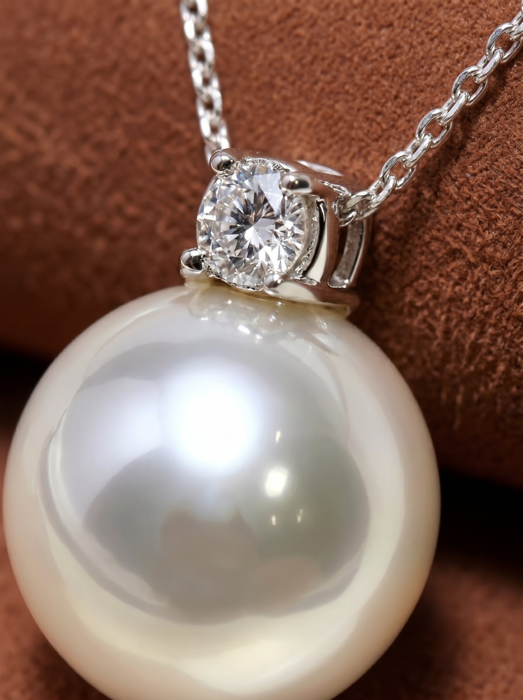 Lumin - South Sea pearl chain drop necklace featuring a large, lustrous pearl and a sparkling diamond set in white gold, on a brown textured background.