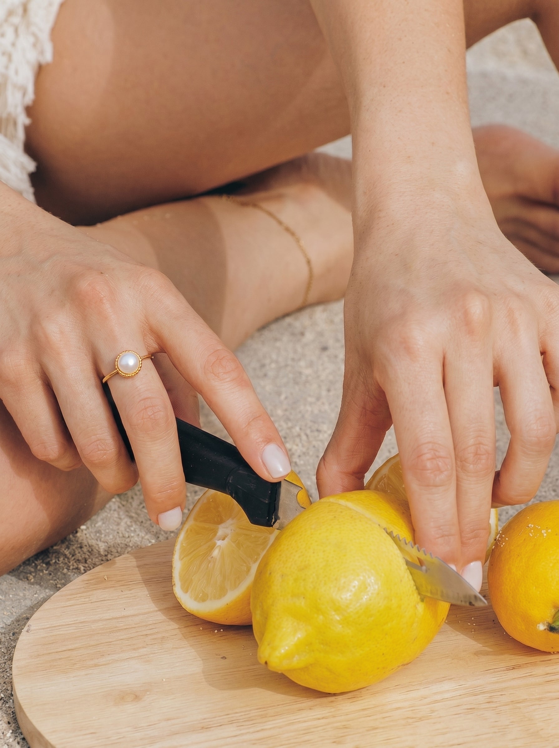 A woman's hand wearing the Lumina Freshwater Pearl Cuff Ring cuts lemons on a wooden board at the beach. @model