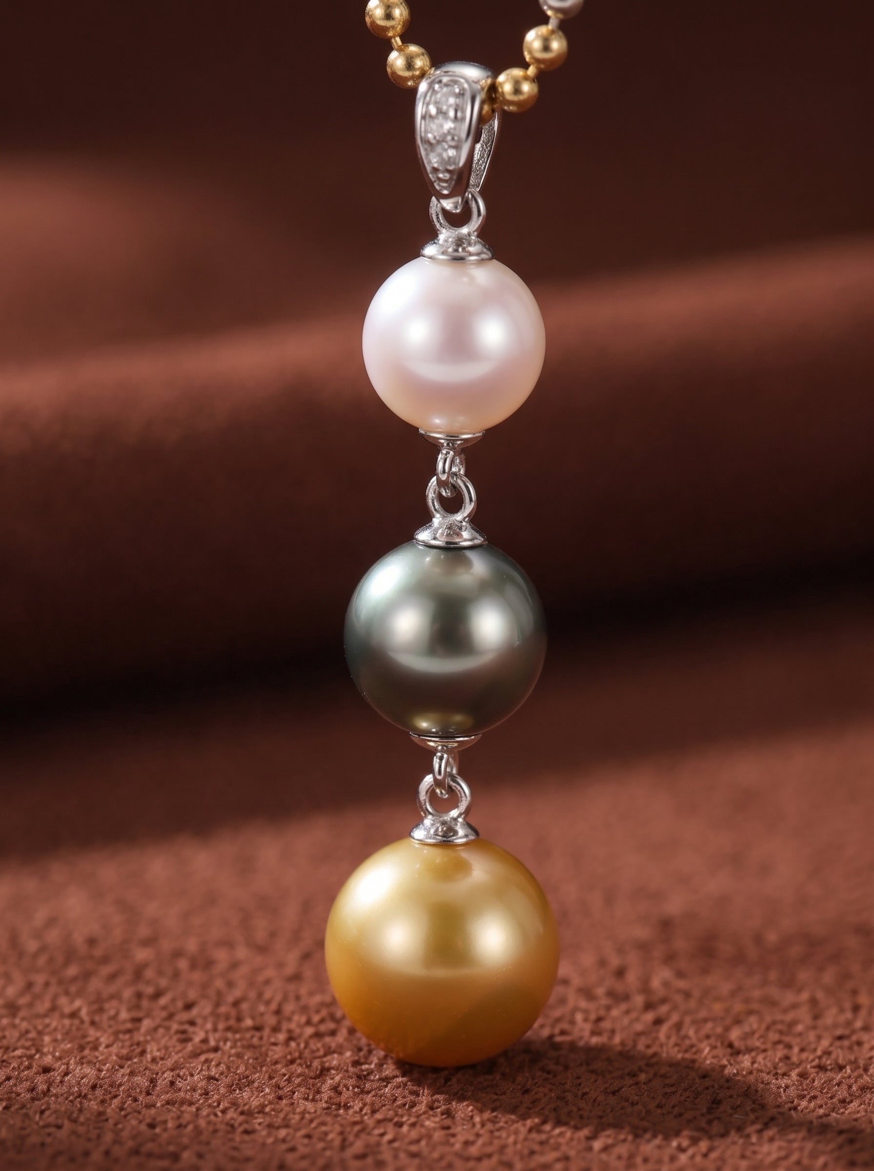 Luminance necklace featuring a vertical drop of three round pearls: a pinkish white Akoya pearl, a dark grey Tahitian pearl, and a golden South Sea pearl, suspended from a mixed-tone ball chain. @pearl