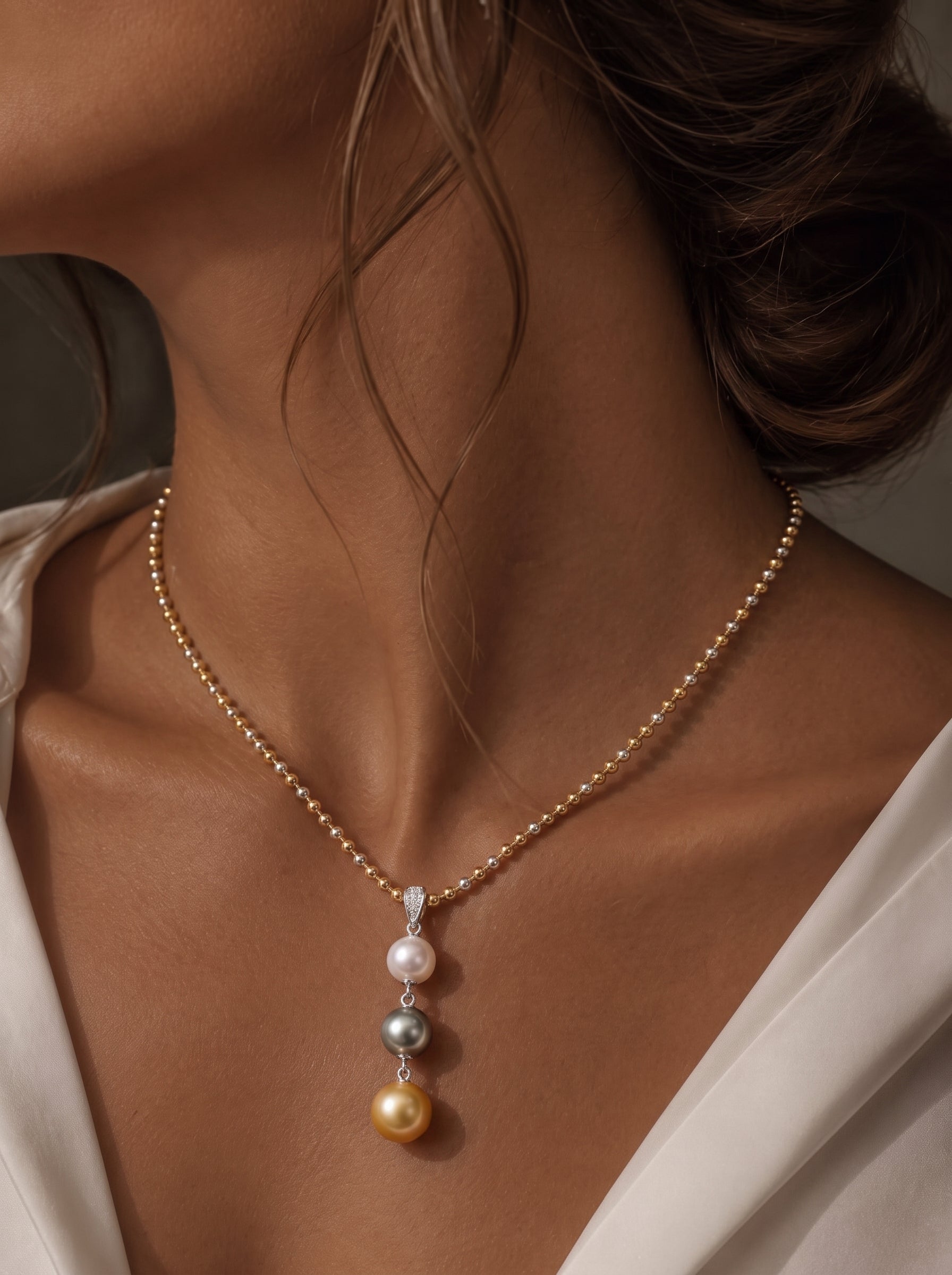 Luminance necklace featuring a white Akoya pearl, a grey Tahitian pearl, and a golden South Sea pearl on a mixed-tone ball chain, worn by a model. @model