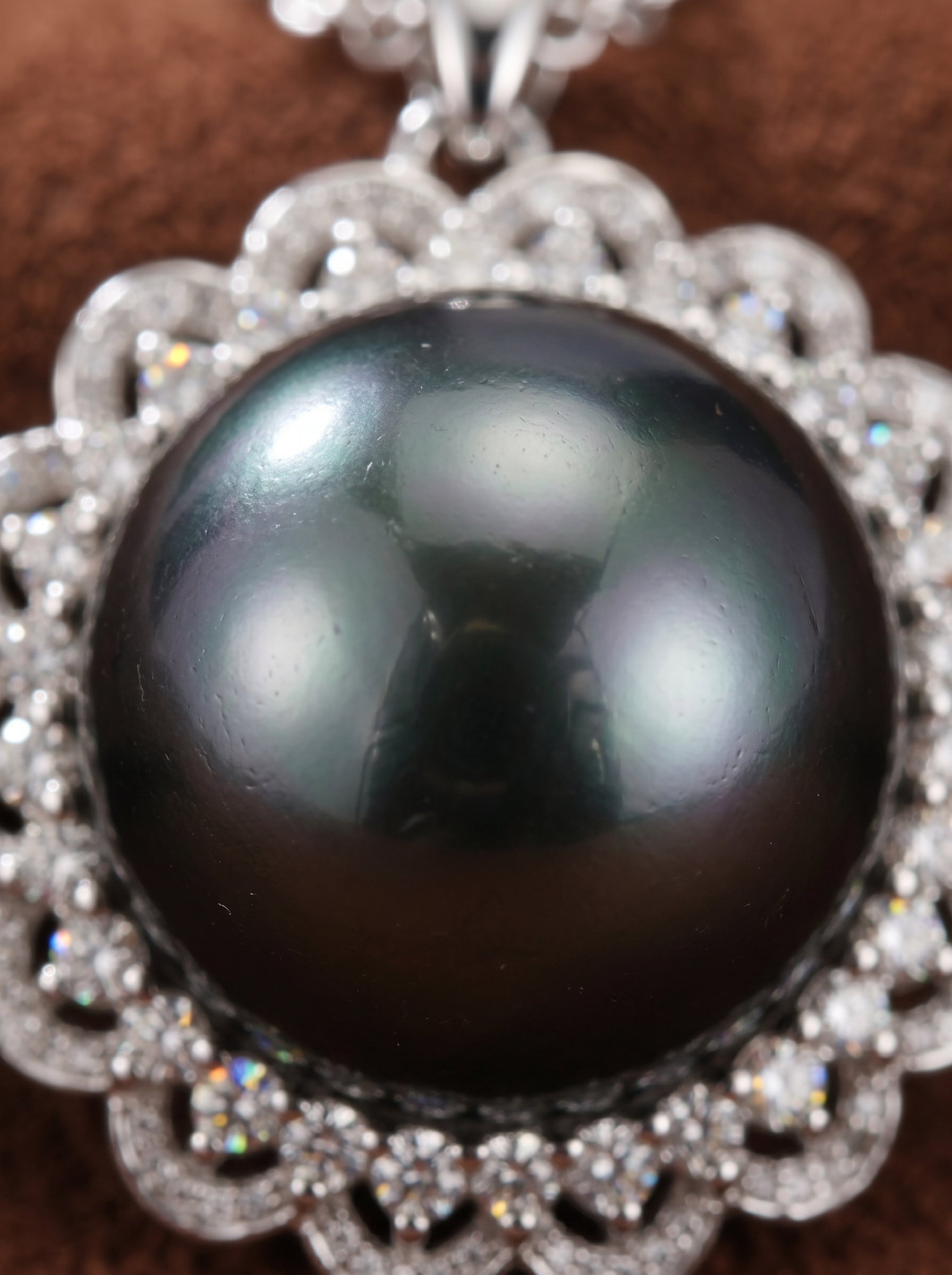 Close up of a Luminary Tahitian Mabe Pearl sun pendant necklace featuring a large, round, black pearl surrounded by a halo of sparkling diamonds set in white gold. @pearl