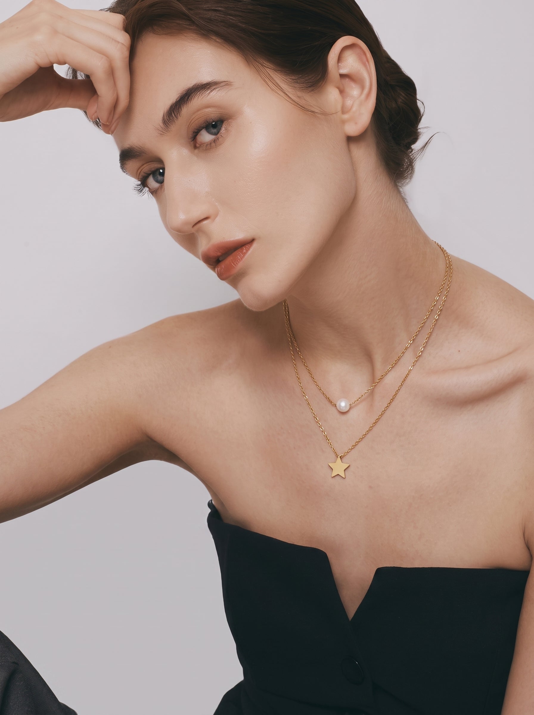 Collier superposé ton or avec une perle blanche d'eau douce sur la chaîne supérieure et une breloque étoile sur la chaîne inférieure, porté par une mannequin. @model