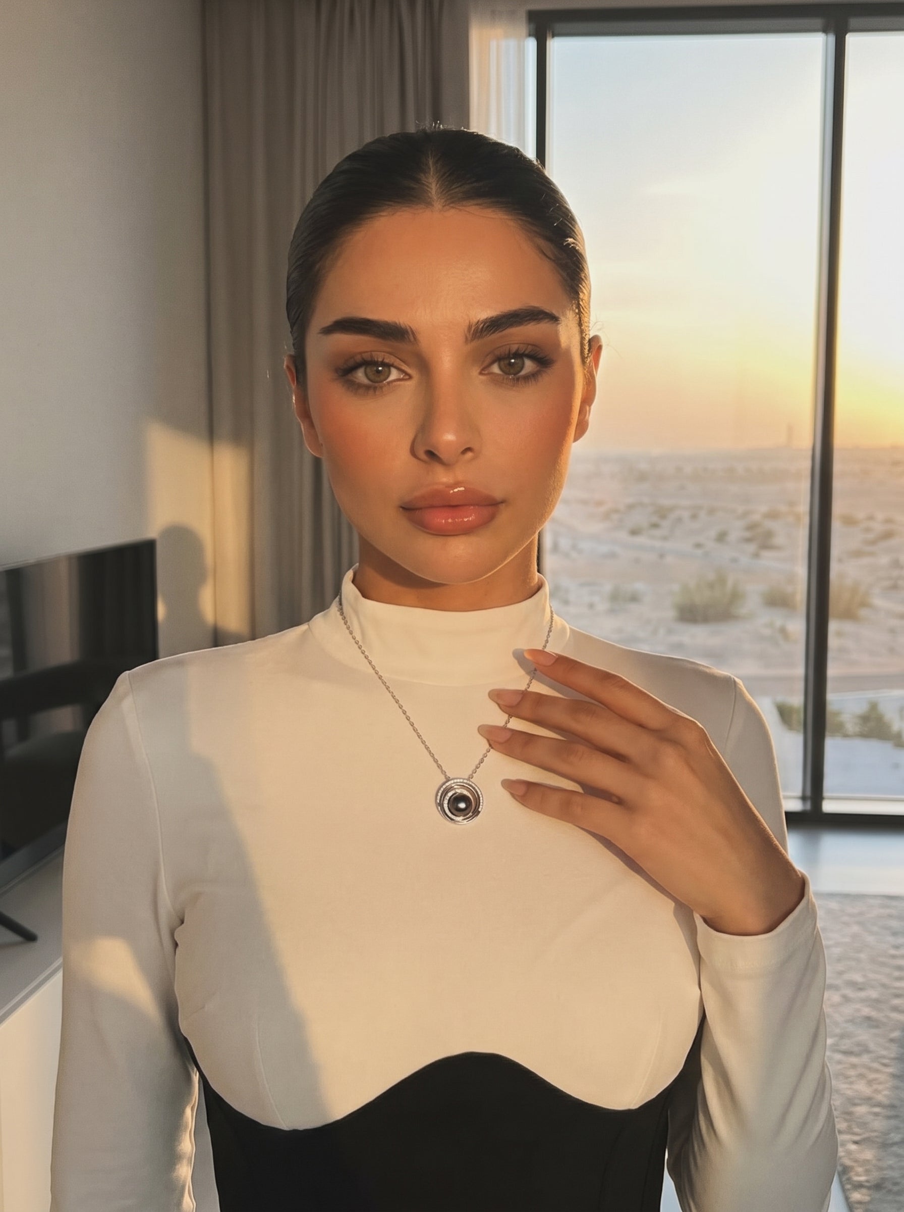 Femme portant le collier pendentif concentrique Lunar Core en perle de Tahiti présentant une perle noire entourée d'anneaux concentriques en argent sterling contre une vue de coucher de soleil. @lifestyle