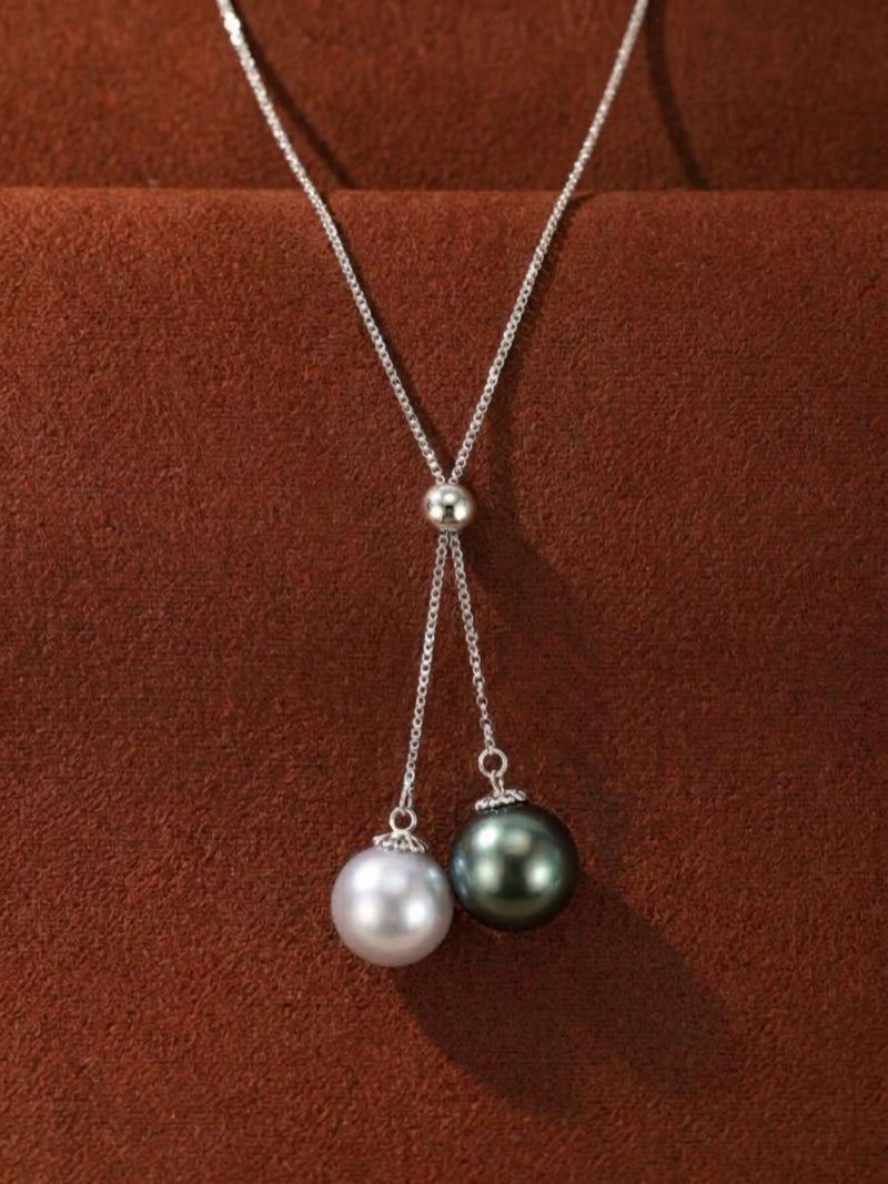 Adjustable sterling silver necklace featuring a Y-drop design with a 10mm luminous white Akoya pearl and an 8mm dark Tahitian pearl against a textured brown background.