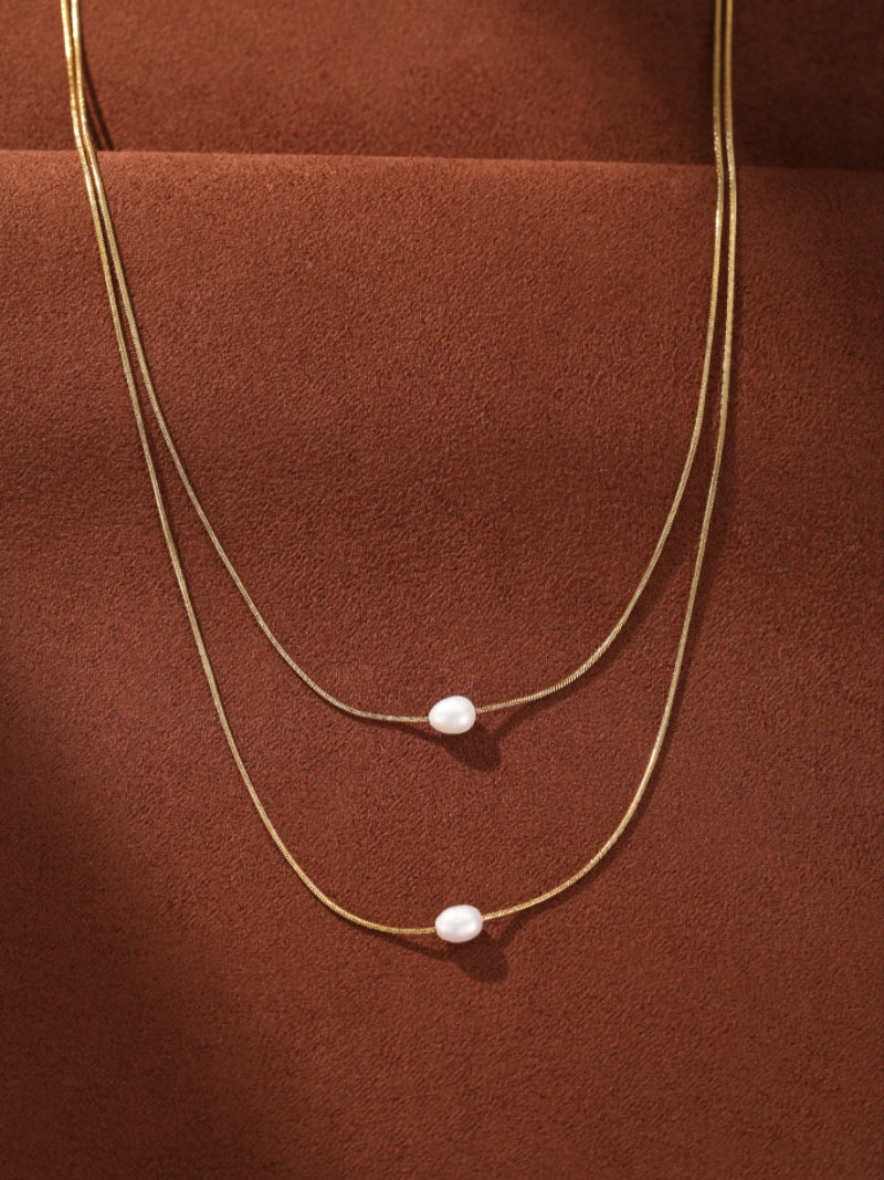 Lunar Glide layered necklace featuring two delicate gold-tone snake chains, each adorned with a single floating freshwater baroque pearl. @pearl