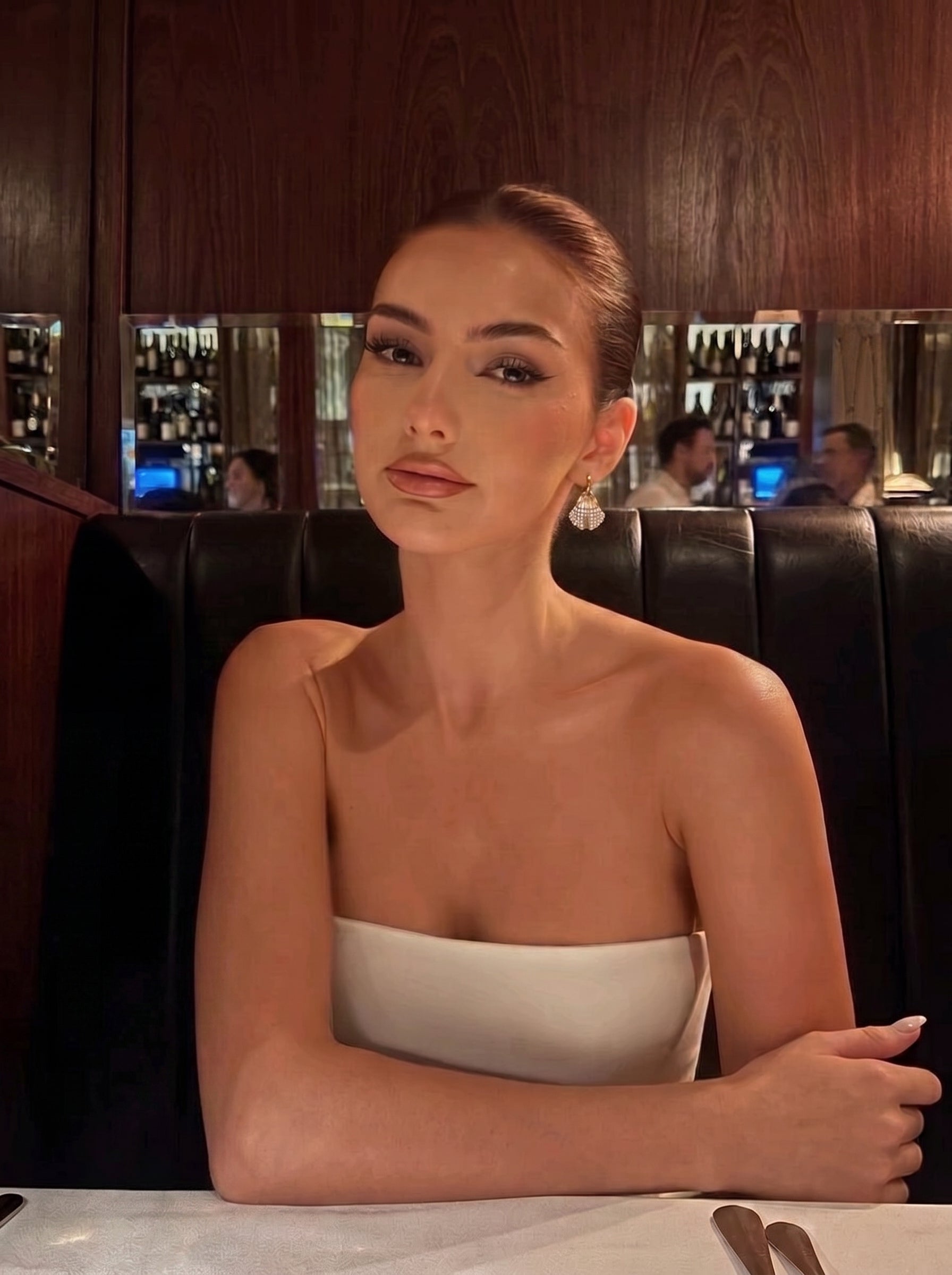 A woman wearing Lush Freshwater Pearl Hoop Earrings in a dimly lit, elegant restaurant setting. The earrings are a prominent feature, catching the light. @lifestyle