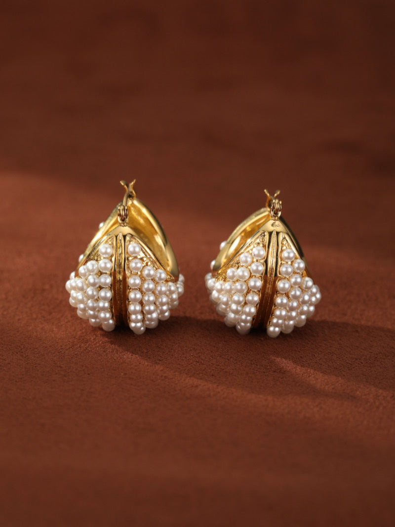 Lush Freshwater Pearl Hoop Earrings feature a unique architectural design adorned with dense arrays of lustrous 2mm white button freshwater pearls. The gold hoops have a textured surface reflecting light, offering a bold yet refined statement.