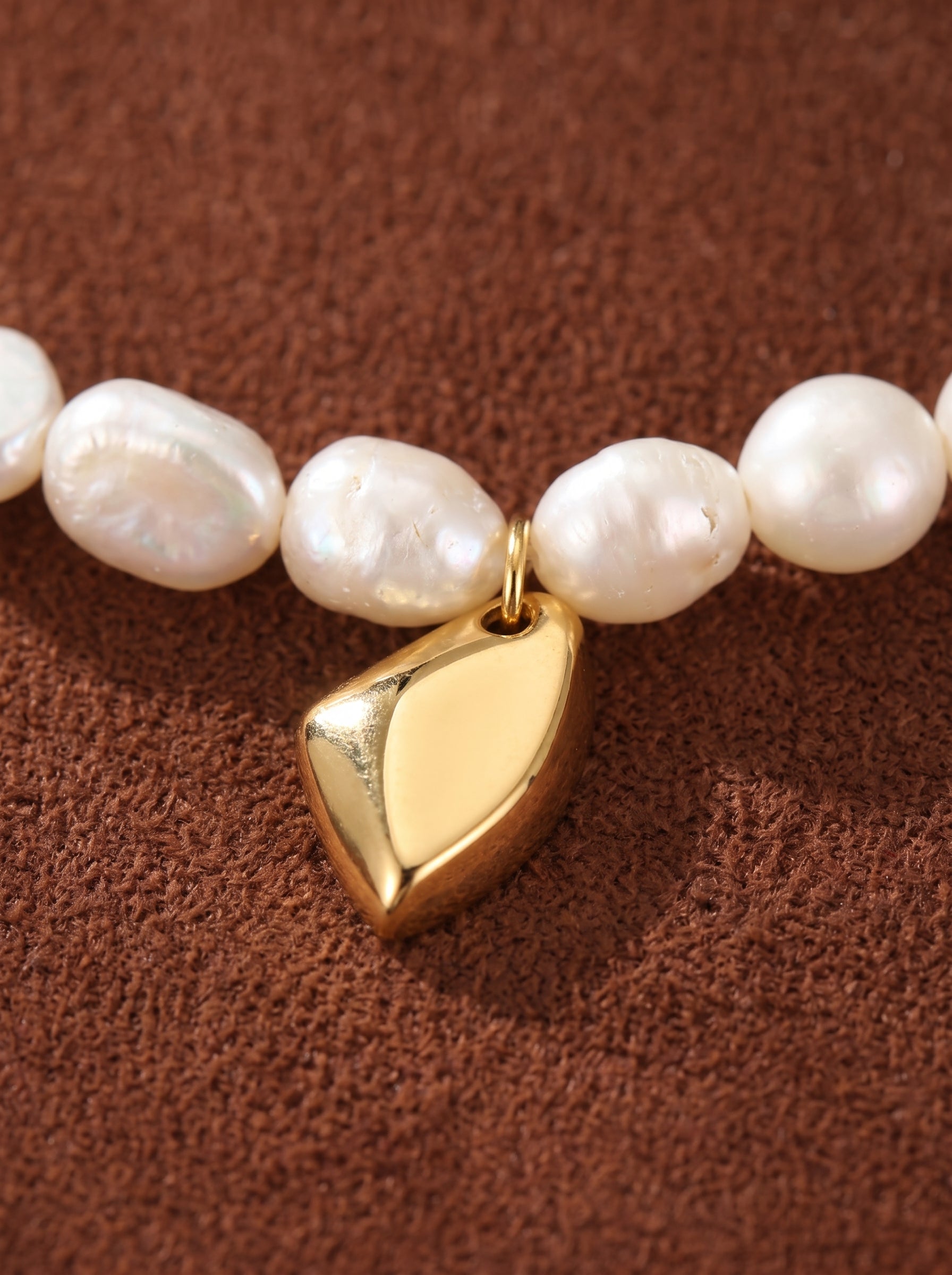 Collier Lyrical présentant un fil de perles blanches irrégulières d'eau douce avec un pendentif goutte abstrait lisse ton or en son centre. @pearl