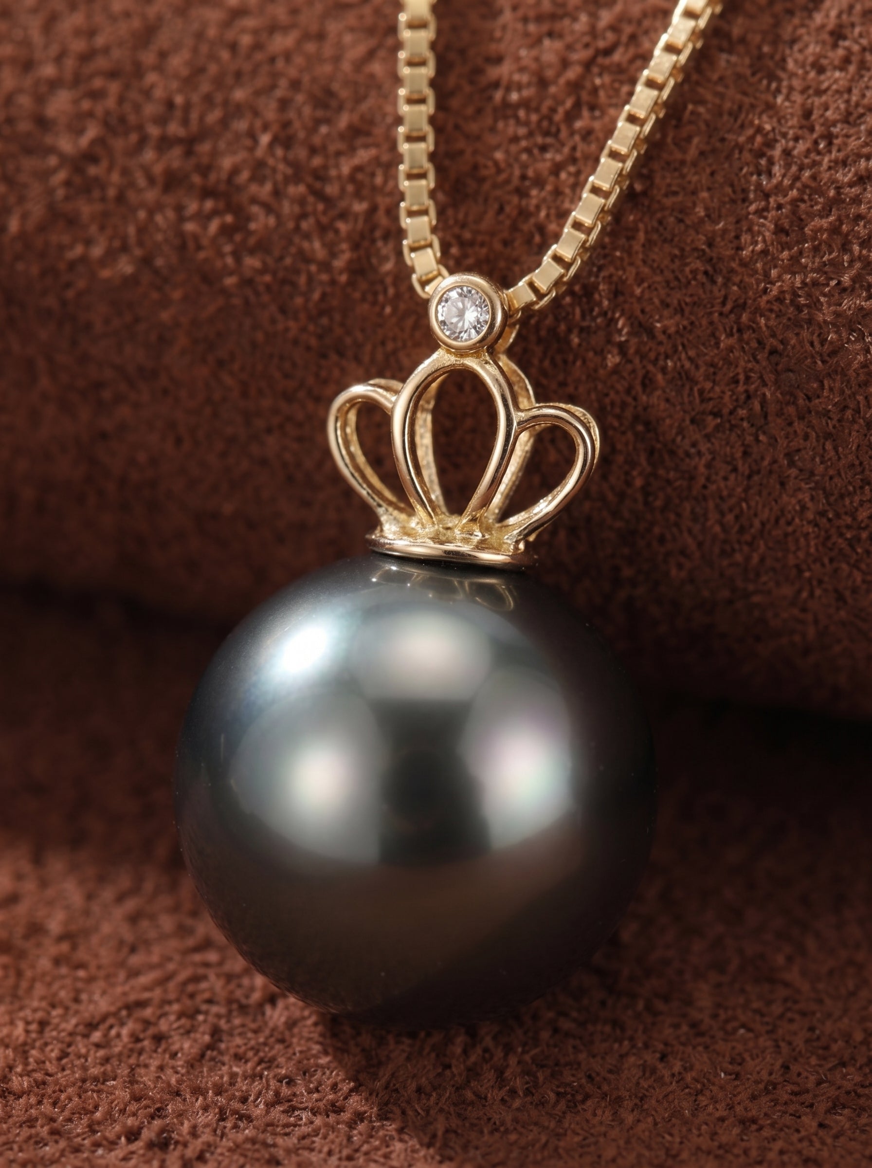 A close-up of the Majesty pendant necklace featuring a large, lustrous Tahitian pearl topped with a golden crown-shaped bail and a small diamond accent. @pearl