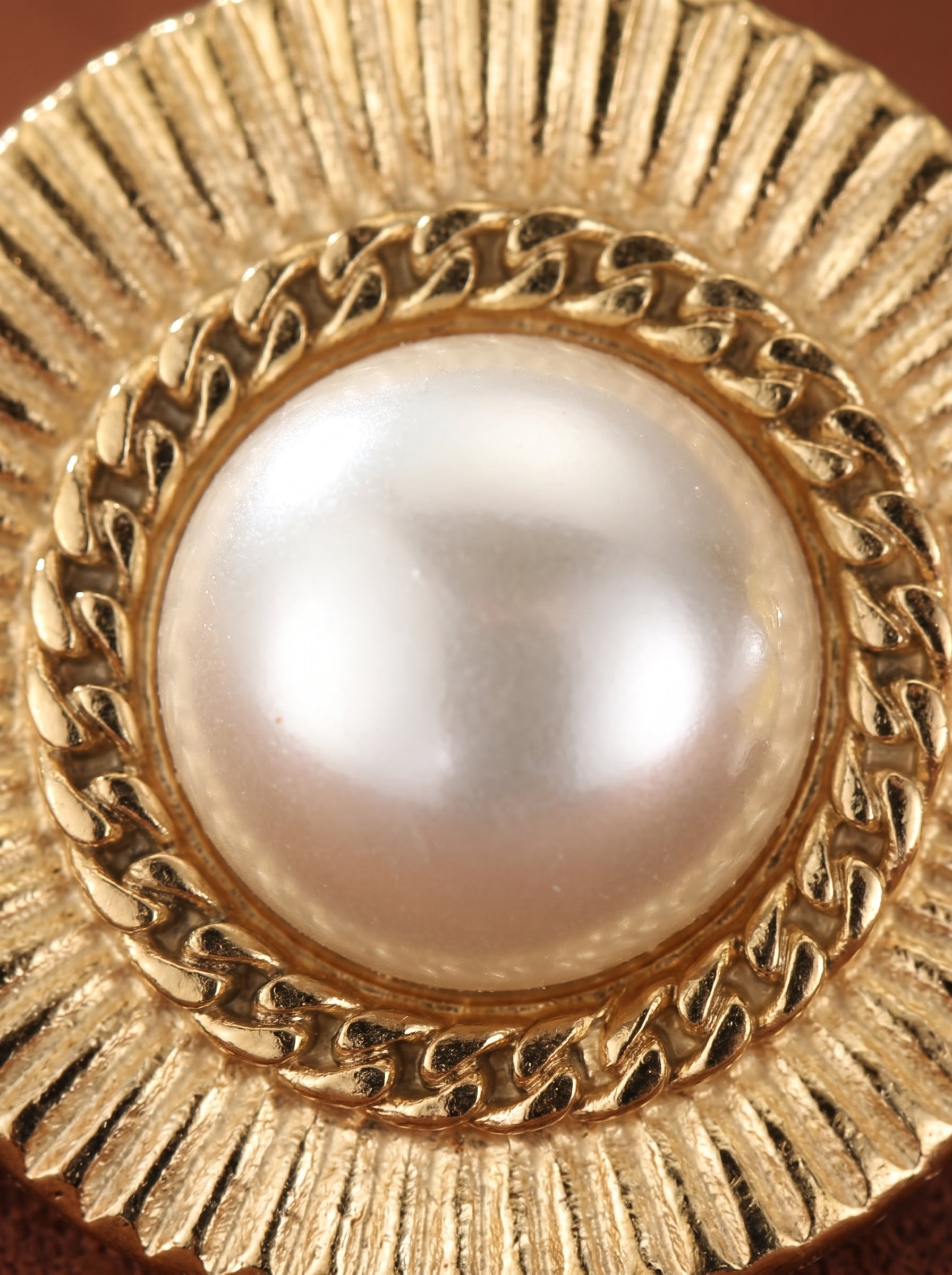 Close-up of a Meridian Shine stud earring featuring a lustrous 12mm freshwater white button pearl set in a gold-toned sunburst frame with textured outer rim and chain-link detail. @pearl