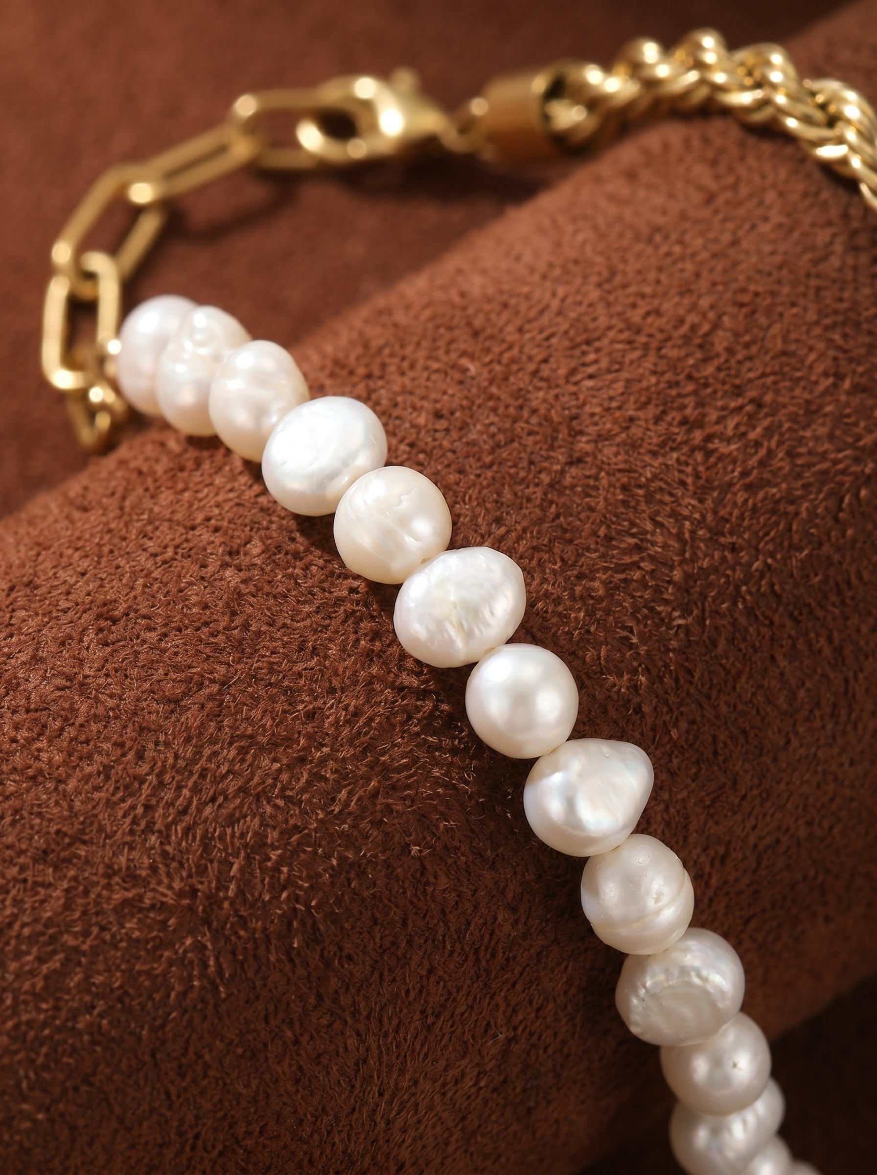 Close-up of a gold-tone chain bracelet with a section of luminous, button-shaped freshwater pearls strung individually. The pearls have a natural luster and irregular shape, contrasting with the polished links of the chain. @pearl