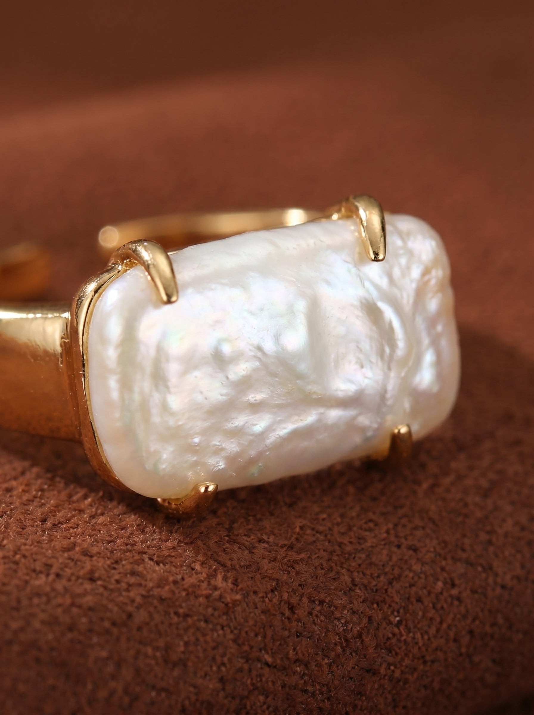 A close-up shot of the Monolith cuff ring, featuring a large, irregular white freshwater baroque pearl set in a modern gold band. The pearl has a lustrous surface with subtle iridescent highlights. @pearl