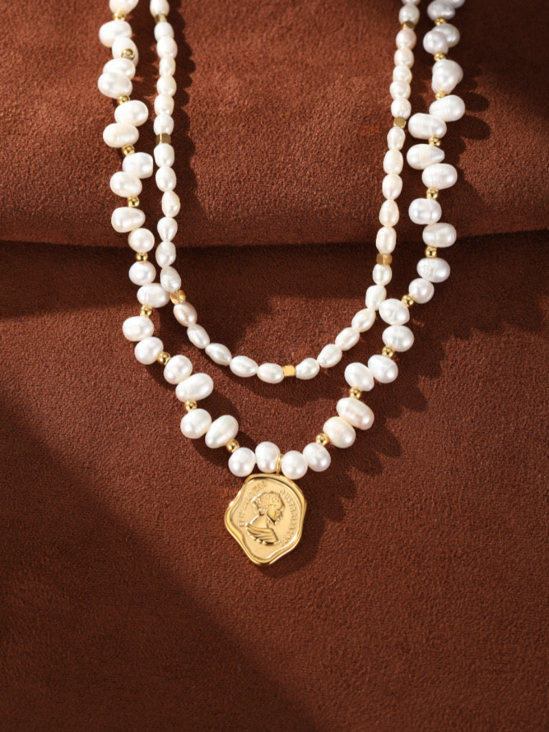 Collier à double rang avec des perles blanches irrégulières d'eau douce et des accents dorés, présentant un pendentif pièce doré avec un portrait de profil.