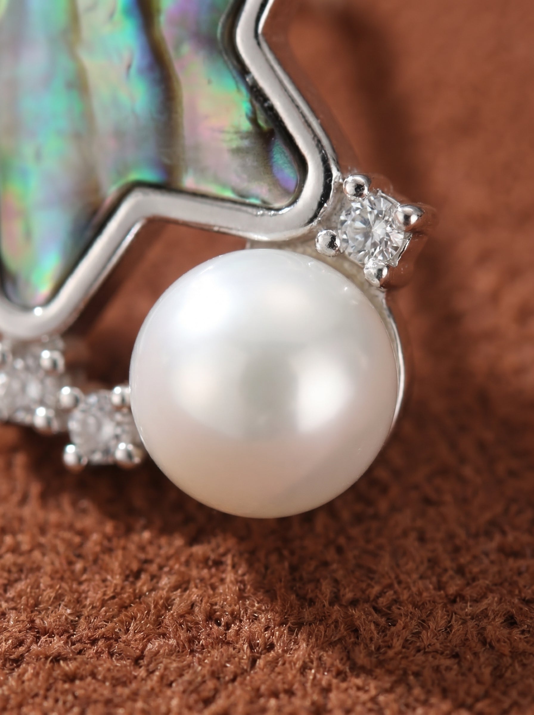 Close-up of a silver stud earring featuring a lustrous white freshwater pearl, iridescent abalone shell in a star shape, and small cubic zirconia stones. @perle
