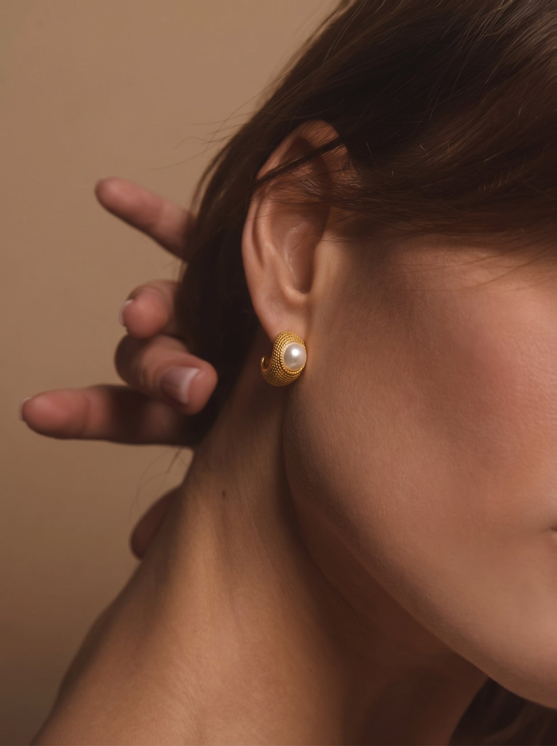 Orbit textured gold-tone stud earrings featuring a white freshwater pearl, shown on a model. @mode