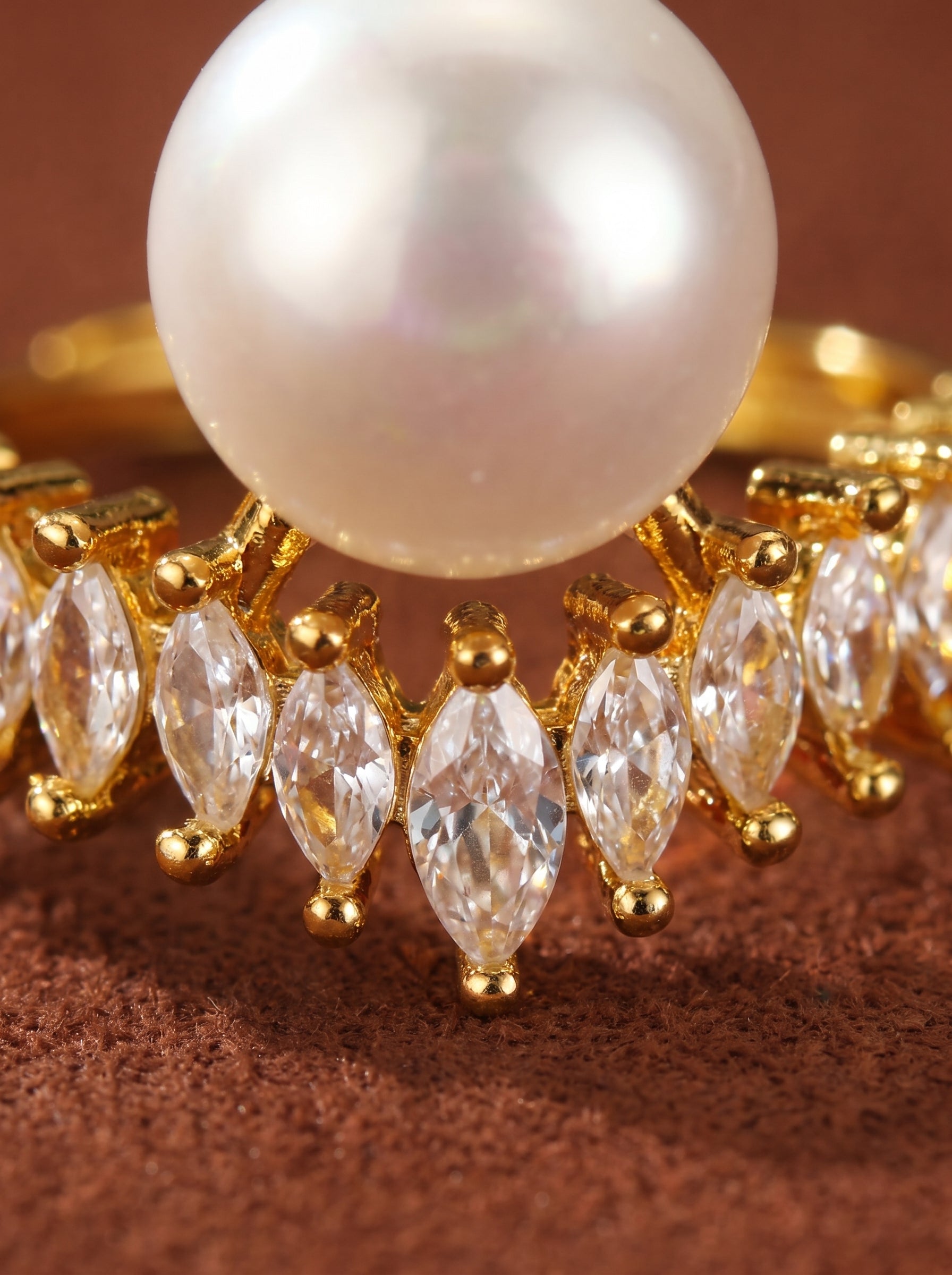 Close-up of a gold cuff ring featuring a large white freshwater button pearl surrounded by marquise-cut clear stones.@pearl