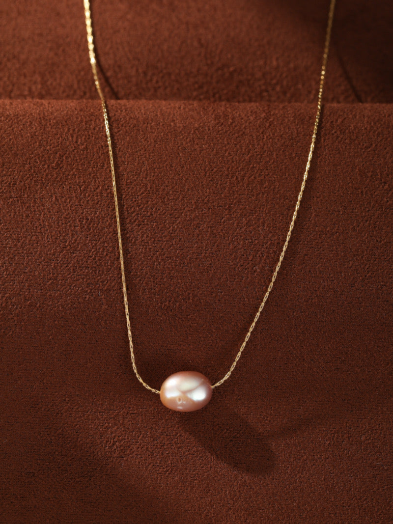 Collier Poise présentant une seule goutte de perle rose sur une fine chaîne dorée, contre un fond texturé marron.