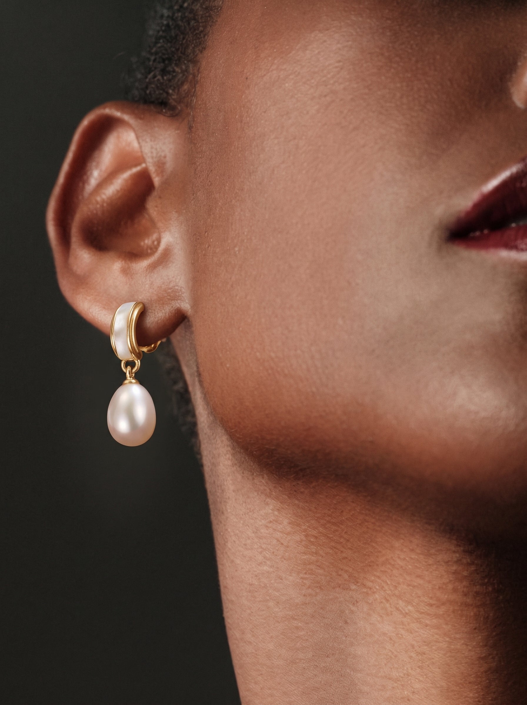 A close-up shot of a model wearing Quietude Freshwater Pearl Drop Earrings, featuring a gold-toned curved element with a white inlay and a single luminous white seed pearl drop. @model