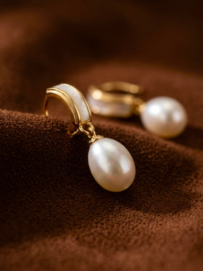 Quietude Freshwater Pearl Drop Earrings featuring a gold-toned curved element with white inlay and a single white seed-shaped pearl drop, luminous 6 mm freshwater pearl drop.