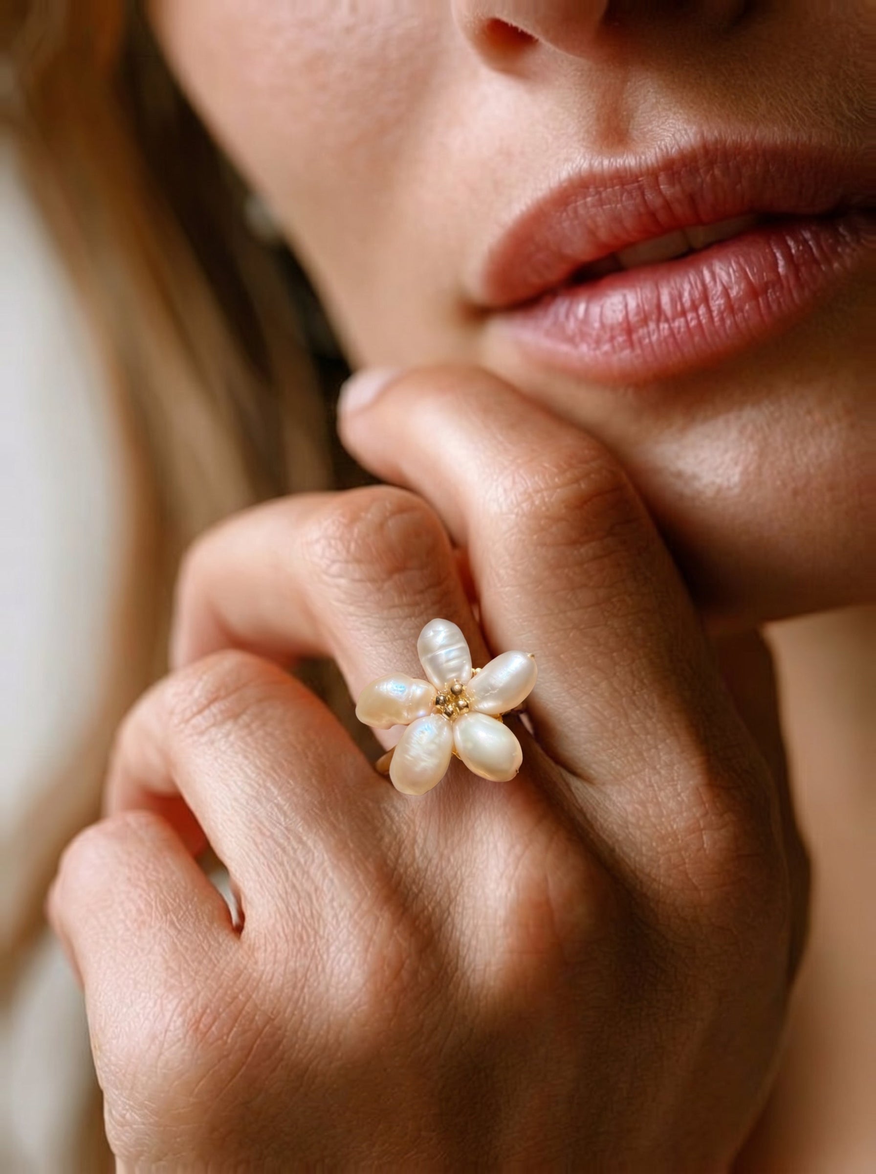 Close-up of a hand wearing a Radiance freshwater pearl flower cuff ring, showcasing its five irregular white baroque pearls arranged like a flower with a small gold bead center. @model