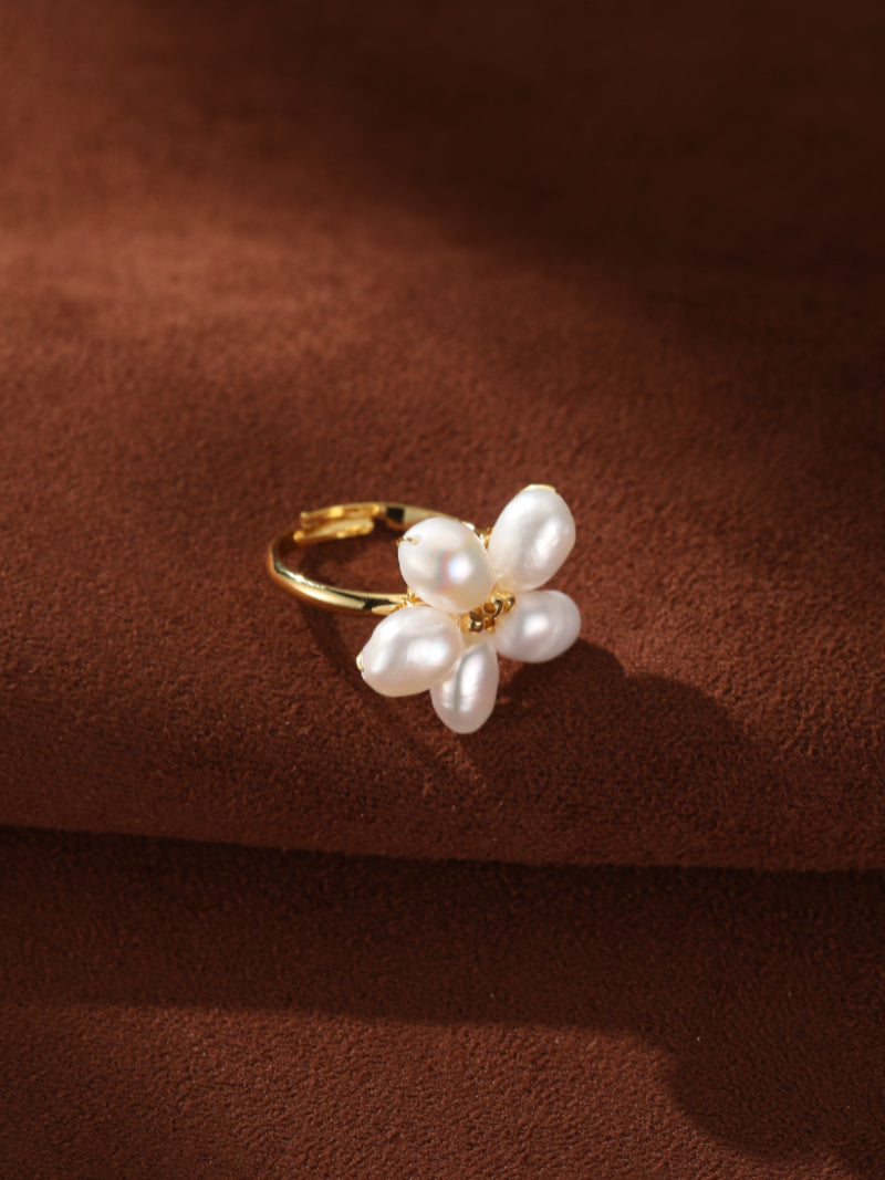A gold cuff ring with a flower design made of five white freshwater baroque pearls against a textured brown background. @pearl