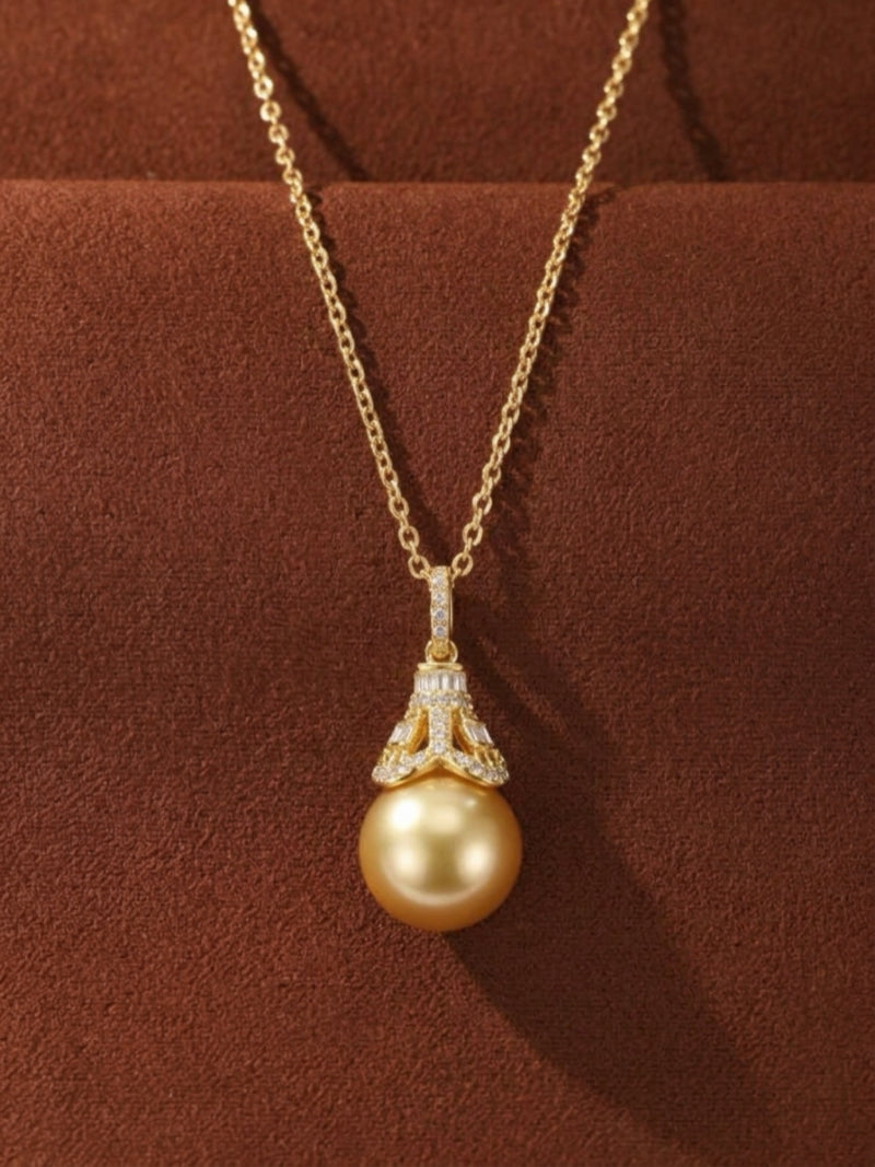 Regal Glow pendant necklace featuring a large, round golden South Sea pearl suspended from a delicate gold chain. The pearl is accented by a diamond-encrusted cap with both round and baguette-cut diamonds.