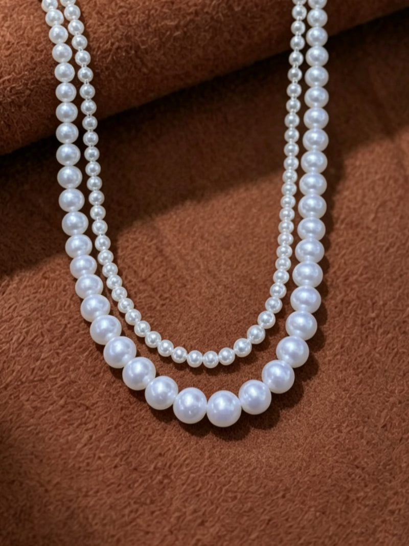 Rhapsody layered necklace featuring two strands of luminous white round freshwater pearls in 5mm and 8mm sizes on a textured brown background.
