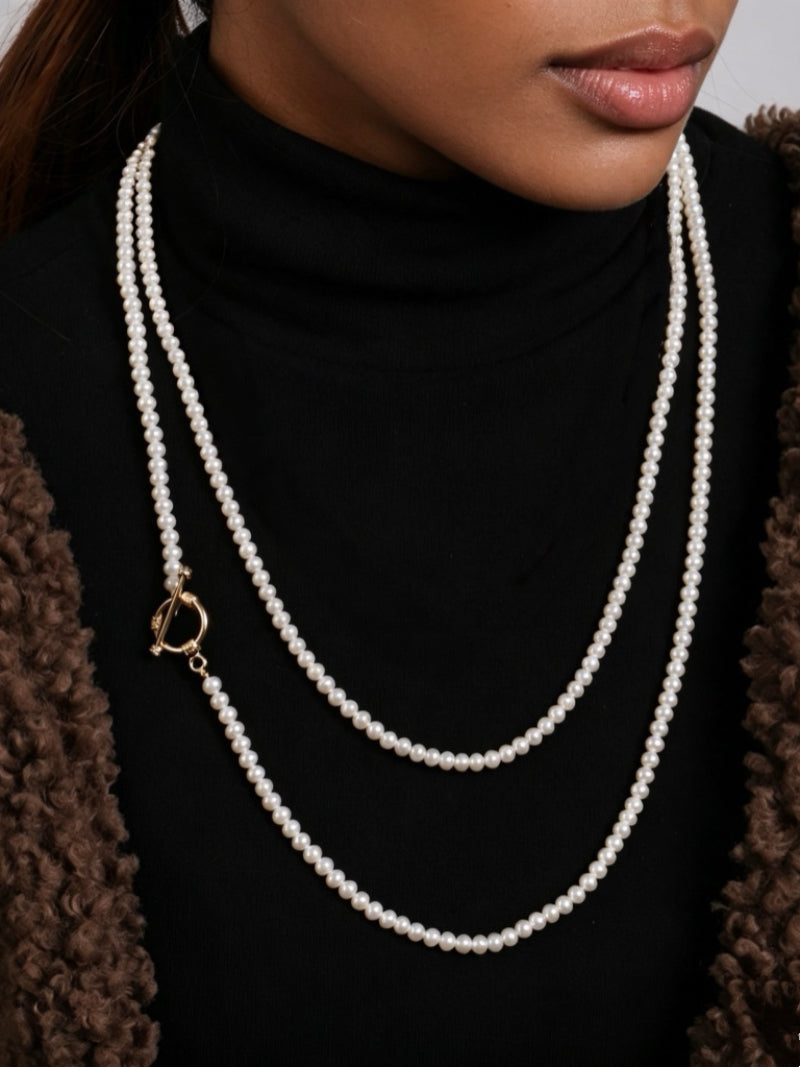 A woman wearing a double-strand freshwater pearl necklace with a gold toggle clasp over a black turtleneck and brown fuzzy jacket. @model